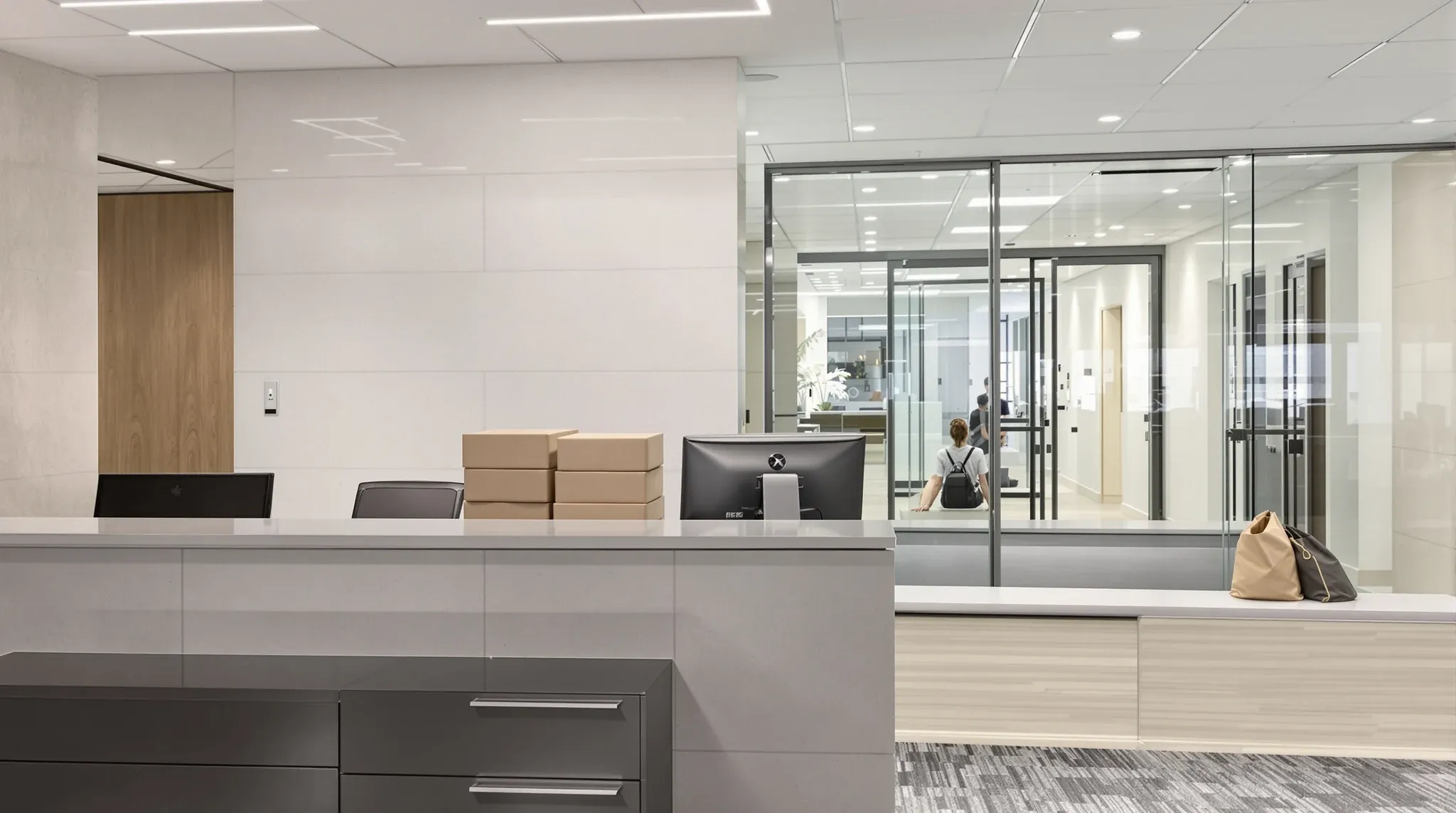 An office reception seen from behind the desk, with visitors waiting by the glass entry