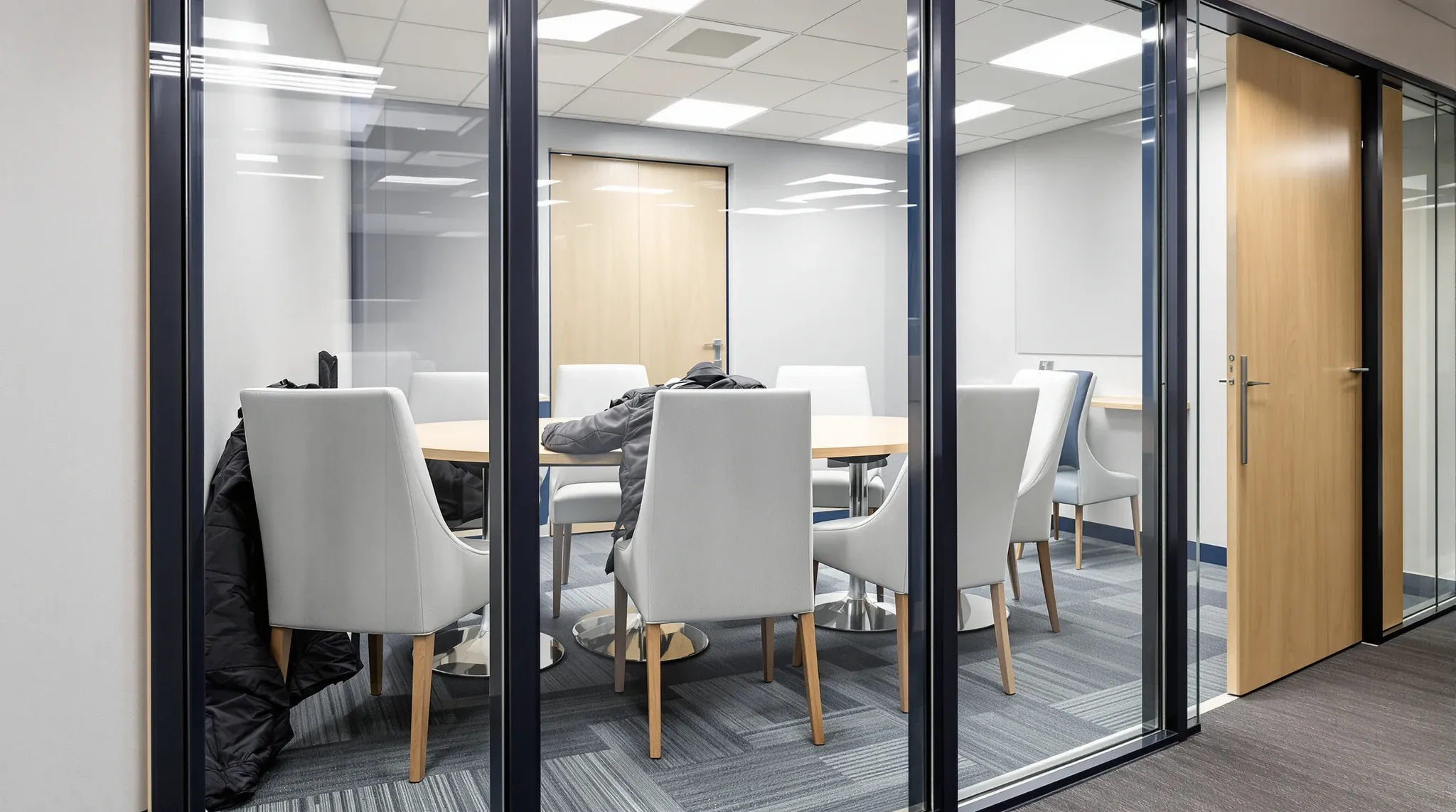 Chairs pressed against the glass wall of a cramped meeting room