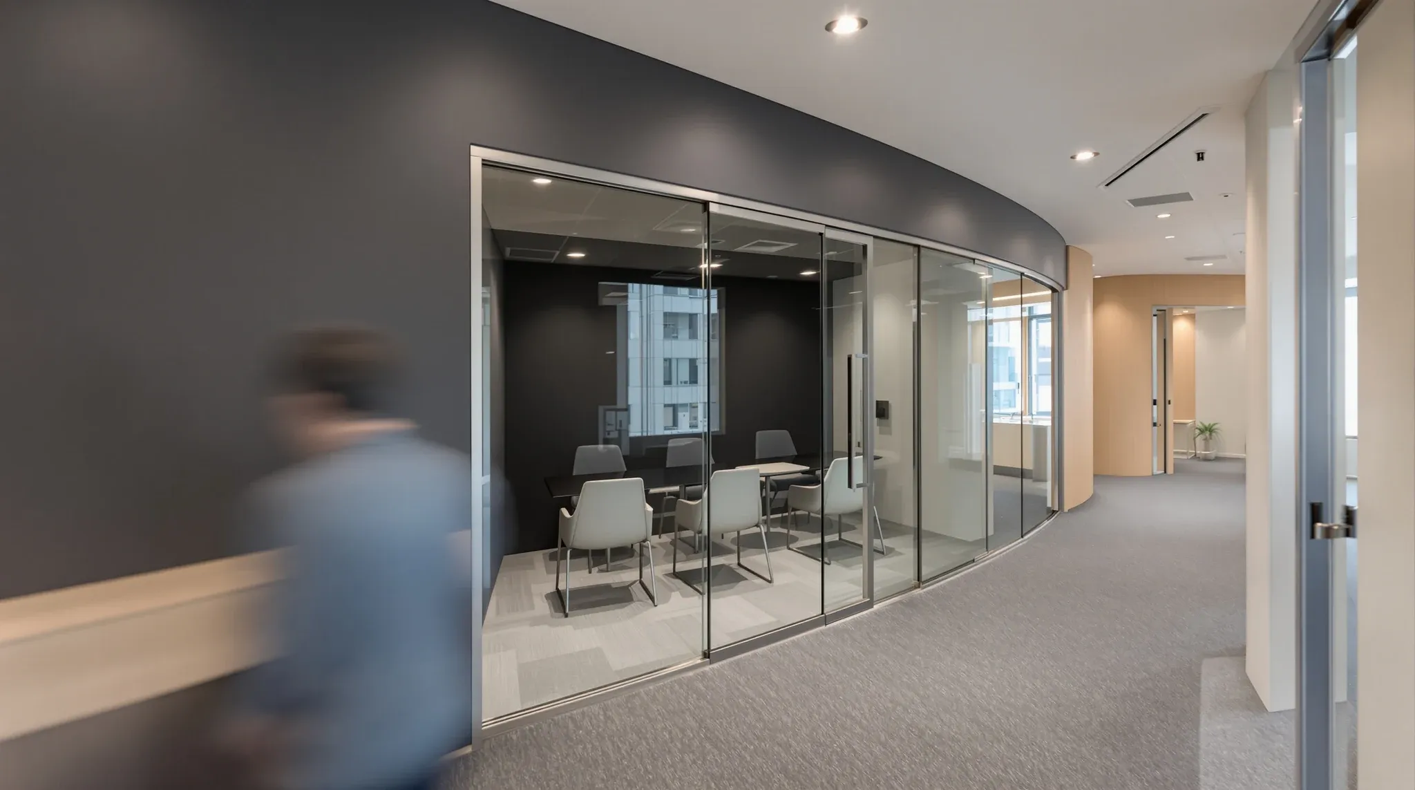 A person working at a corridor ledge beside a dark, empty meeting room on an office floor