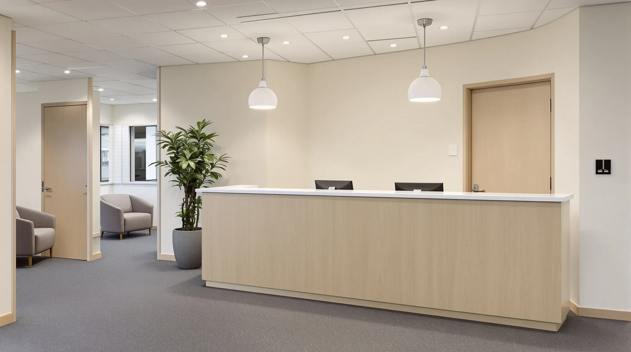 A modest refurbished office reception with an oak counter, limewash wall and two pendant lights