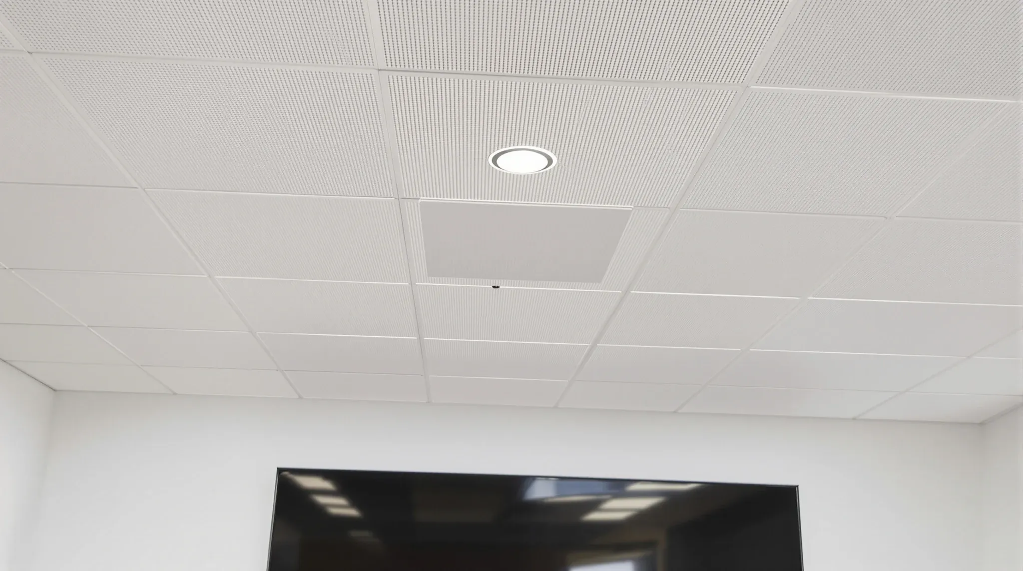 A meeting room ceiling with a microphone tile and speakers set into the existing grid