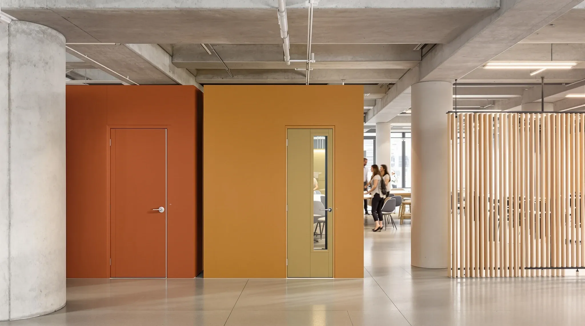 An office floor with coloured doors to small focus rooms beside an open collaboration area