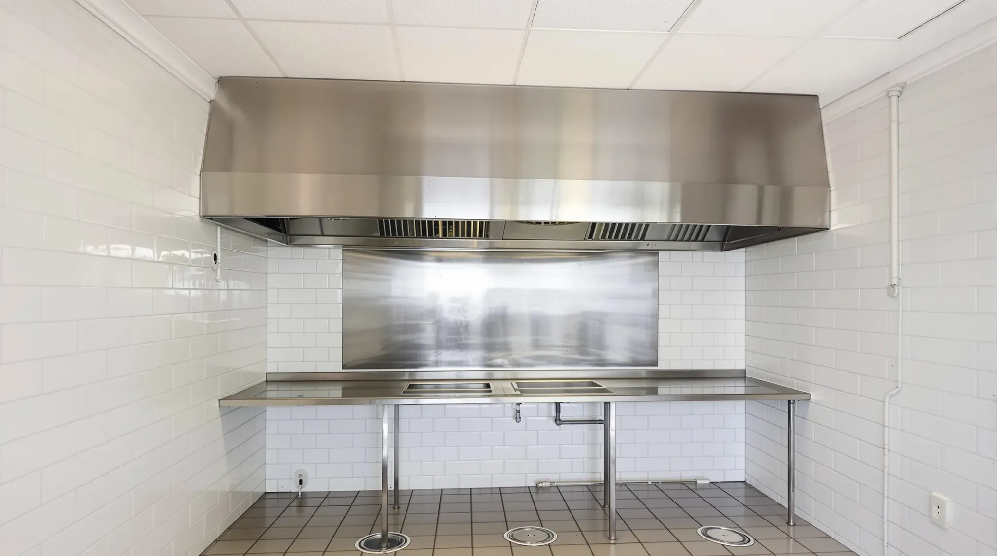 Empty restaurant kitchen before strip out, with a stainless exhaust hood, tiled walls and floor wastes