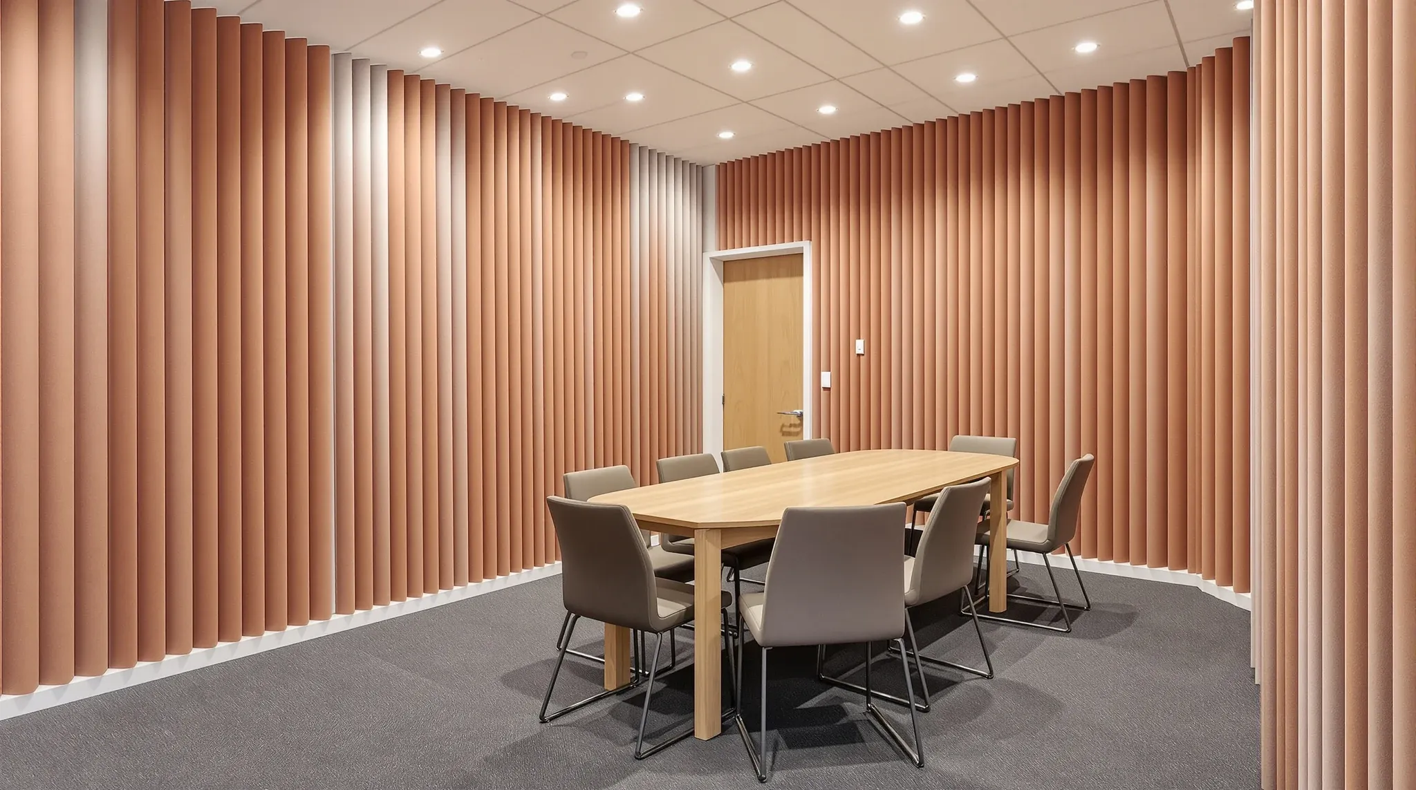 A closed meeting room with rust fabric acoustic wall panels, thick carpet and its solid timber door shut