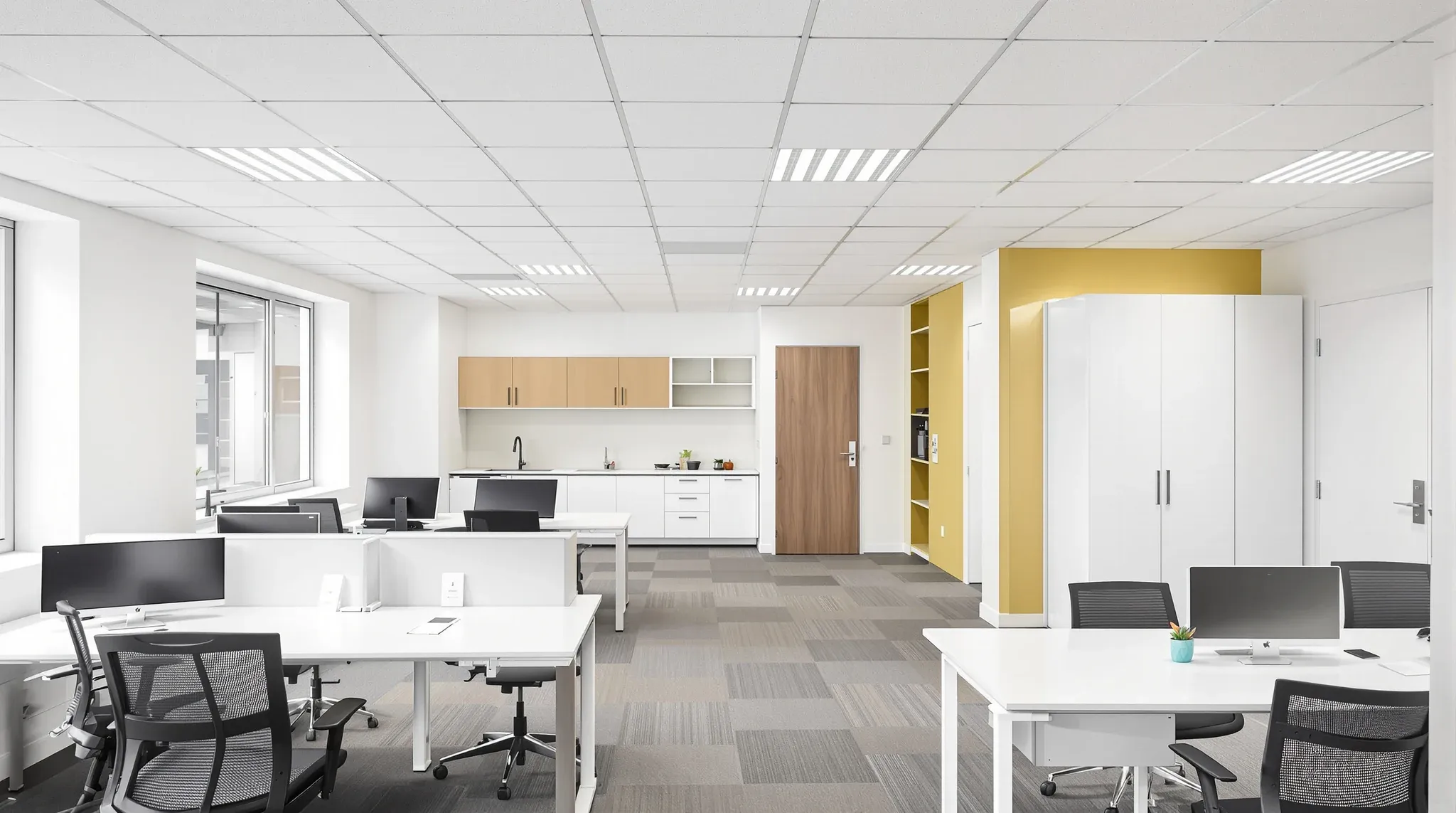 A compact small business office with six desks in two rows and a kitchenette, seen from a high corner