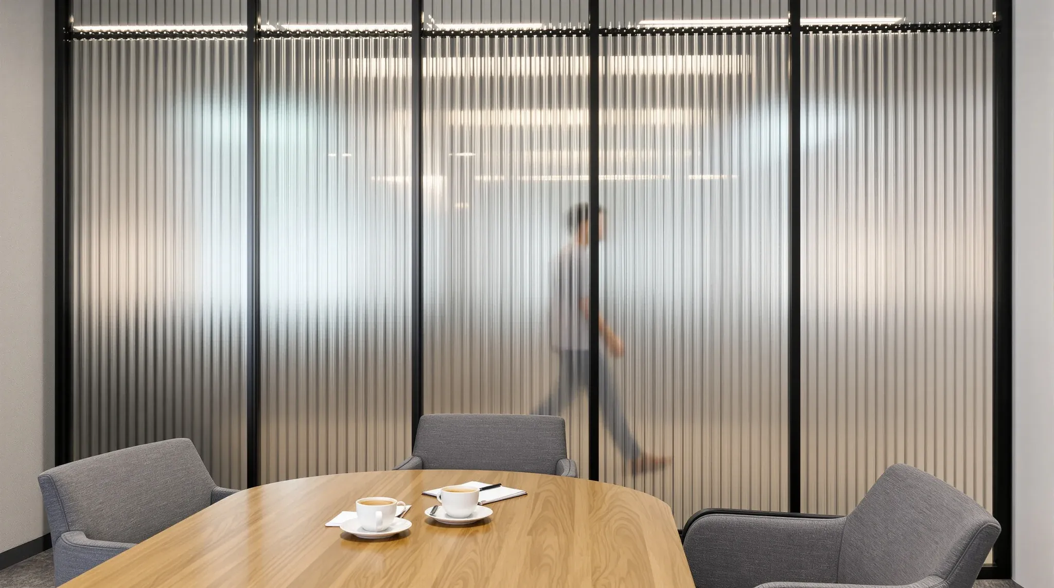 Meeting room with a reeded glass partition softening the view of people and desks beyond