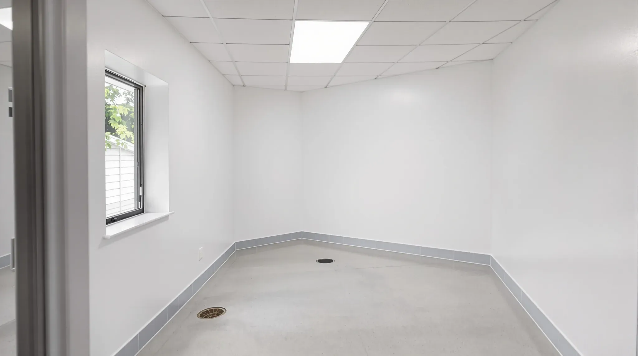 Empty former vet clinic room after make good, with painted walls, a coved skirting, floor drains and a window