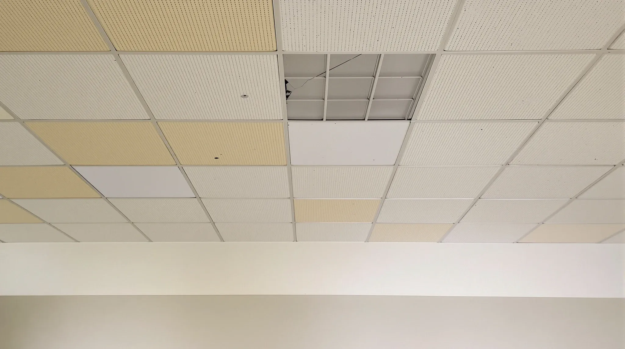A worn office ceiling with yellowed, mismatched and cracked tiles in a vacated tenancy
