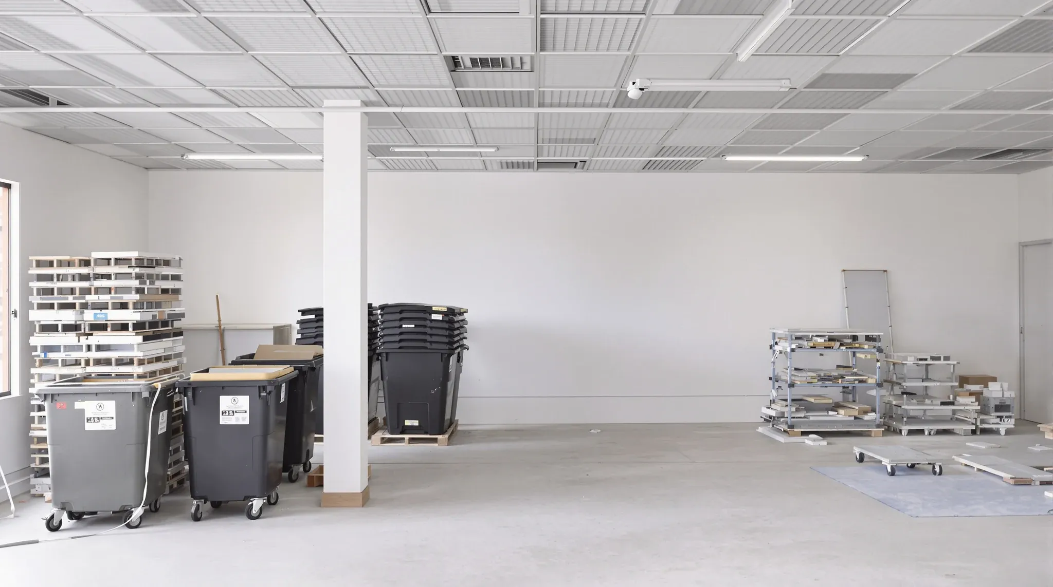Skip bins and stacked ceiling grid in a stripped office floor, no branding