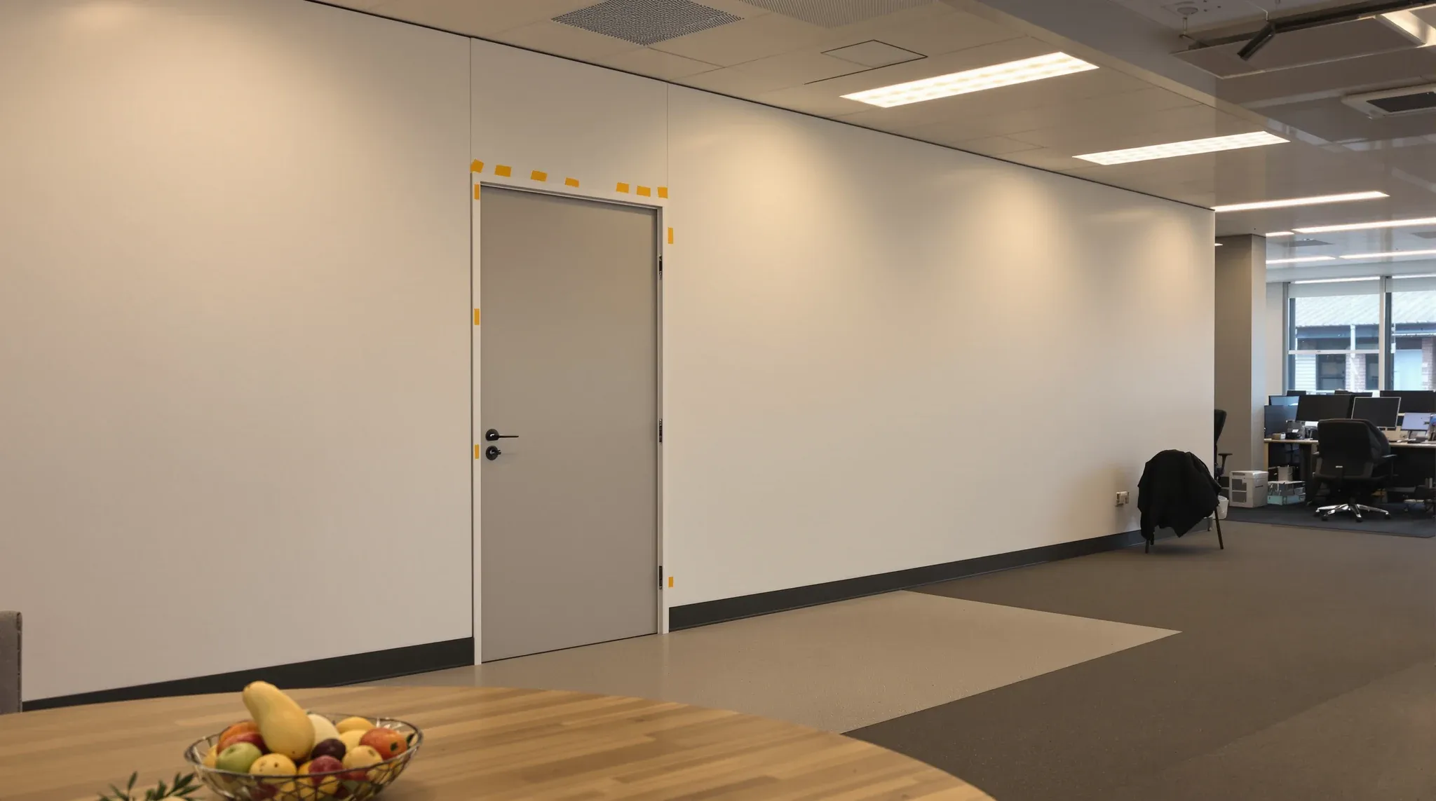 A working office floor with the far end closed off behind a plain white temporary wall and door