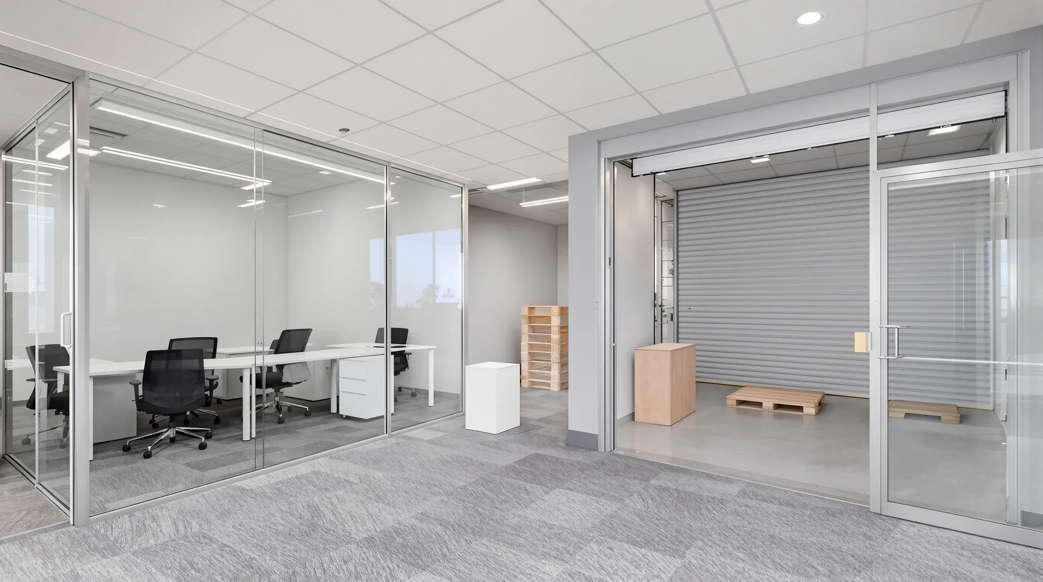 A small ground-floor office looking through a glass wall into a dispatch bay with a closed roller door