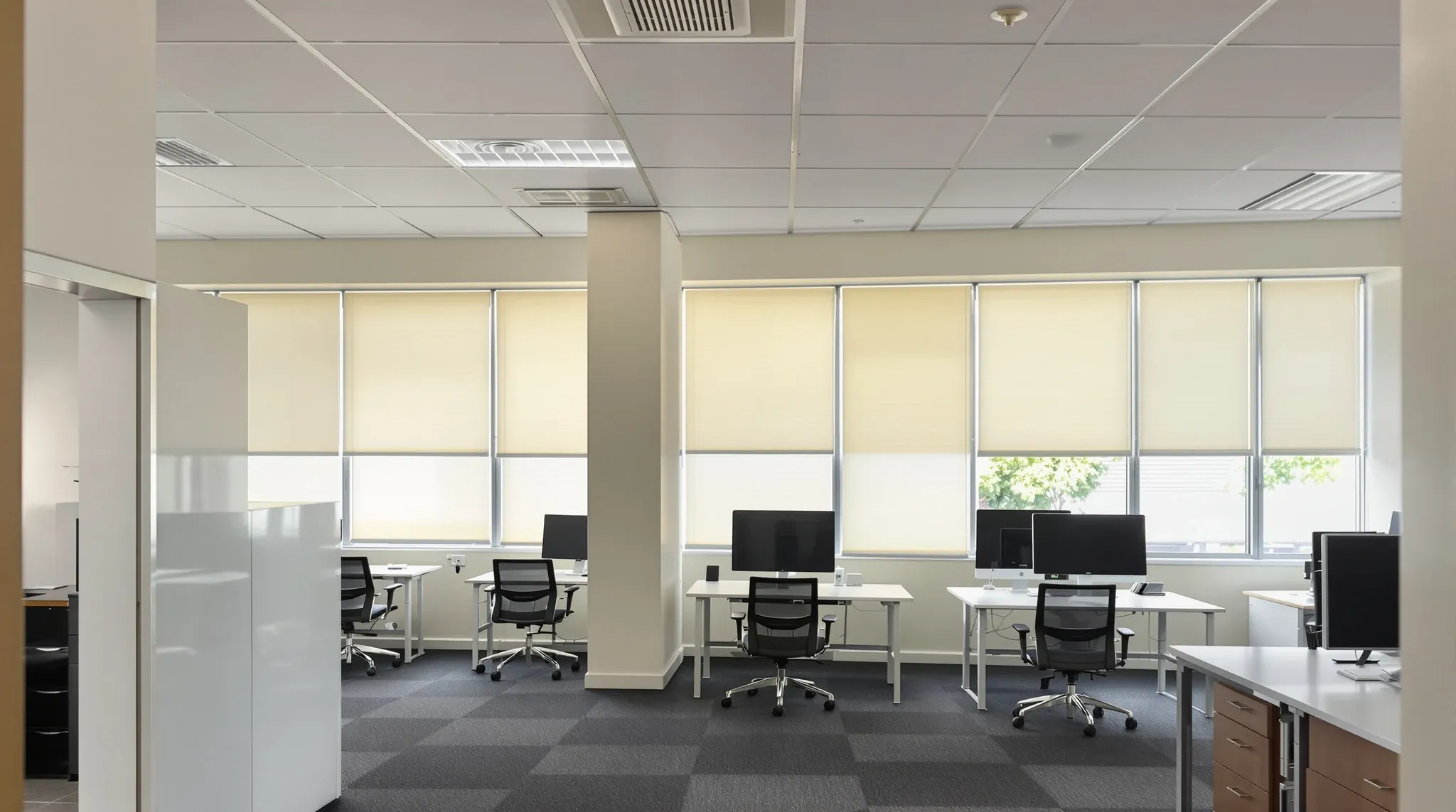 A compact second-floor office suite with desks and a small meeting room, venetian blinds lowered