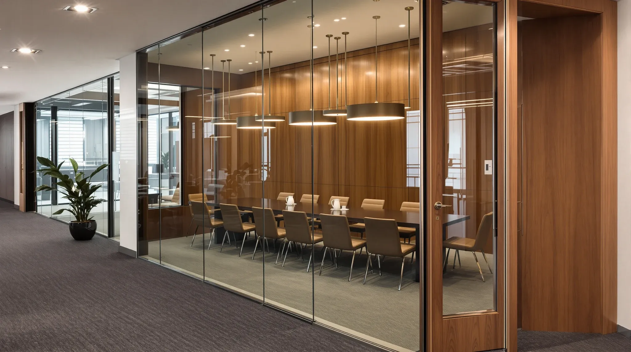 A dim boardroom seen from the corridor through its full-height glass front after dusk
