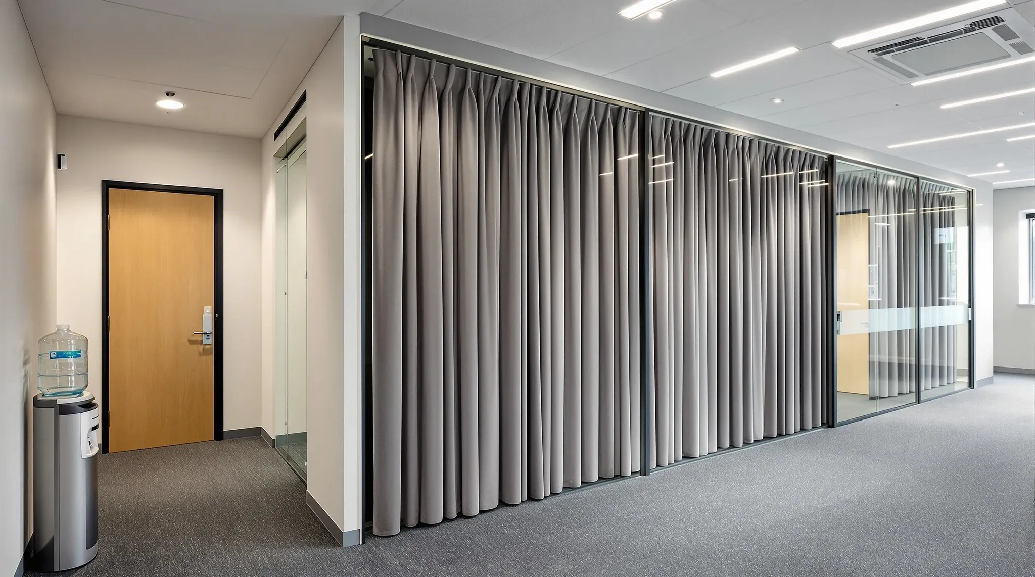 A row of meeting rooms of different sizes with solid doors and glass sidelights, one with a curtain drawn