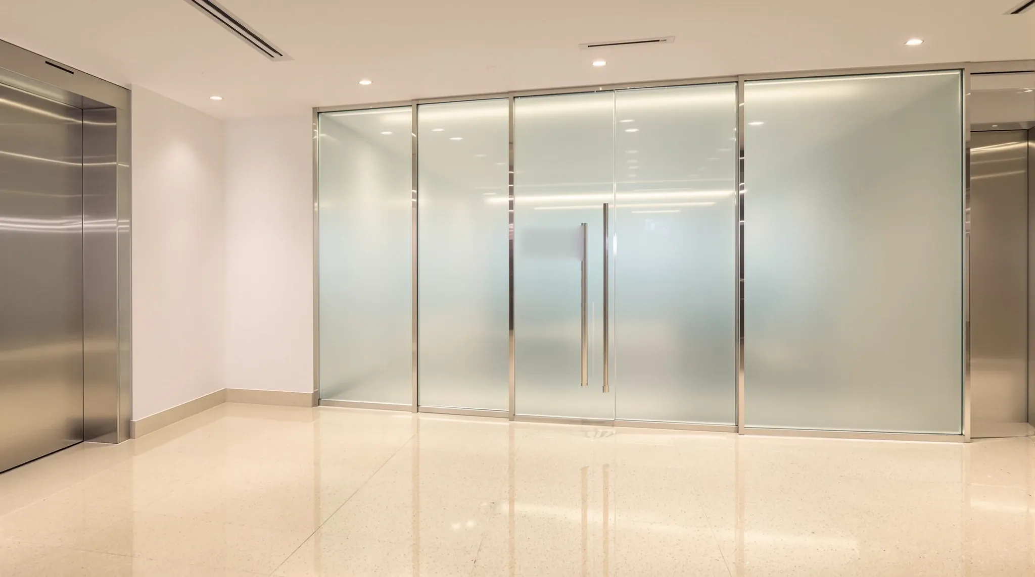A frosted glass tenancy entry with a single glass door facing a stone-floored lift lobby