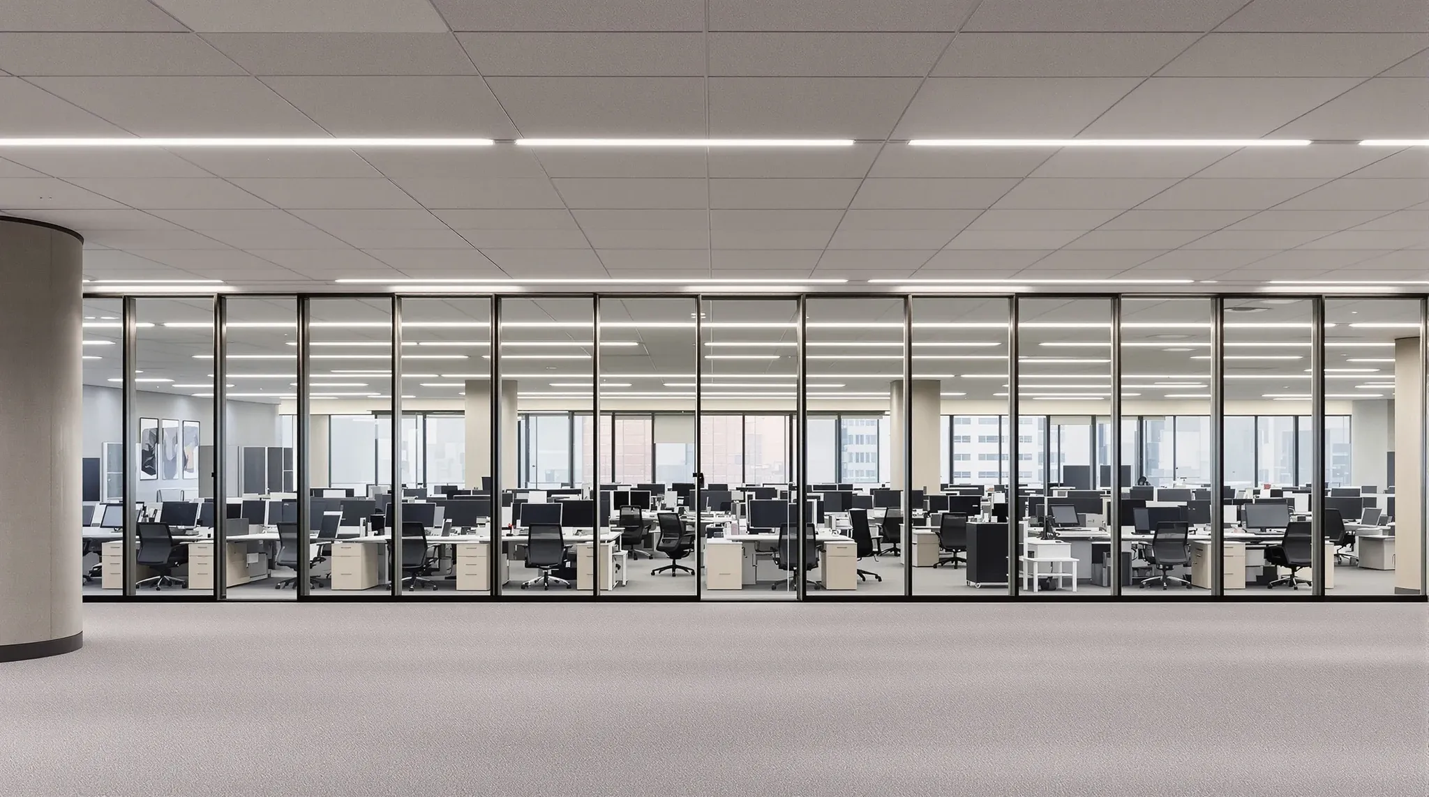 A long run of framed glass offices across the middle of an office floor, seen past workstations
