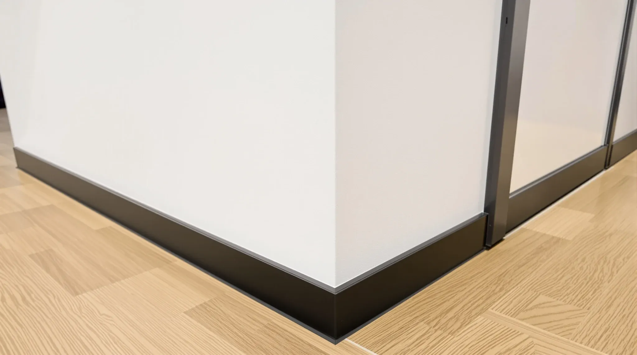 A crisp recessed shadow line where a painted office wall meets a timber floor