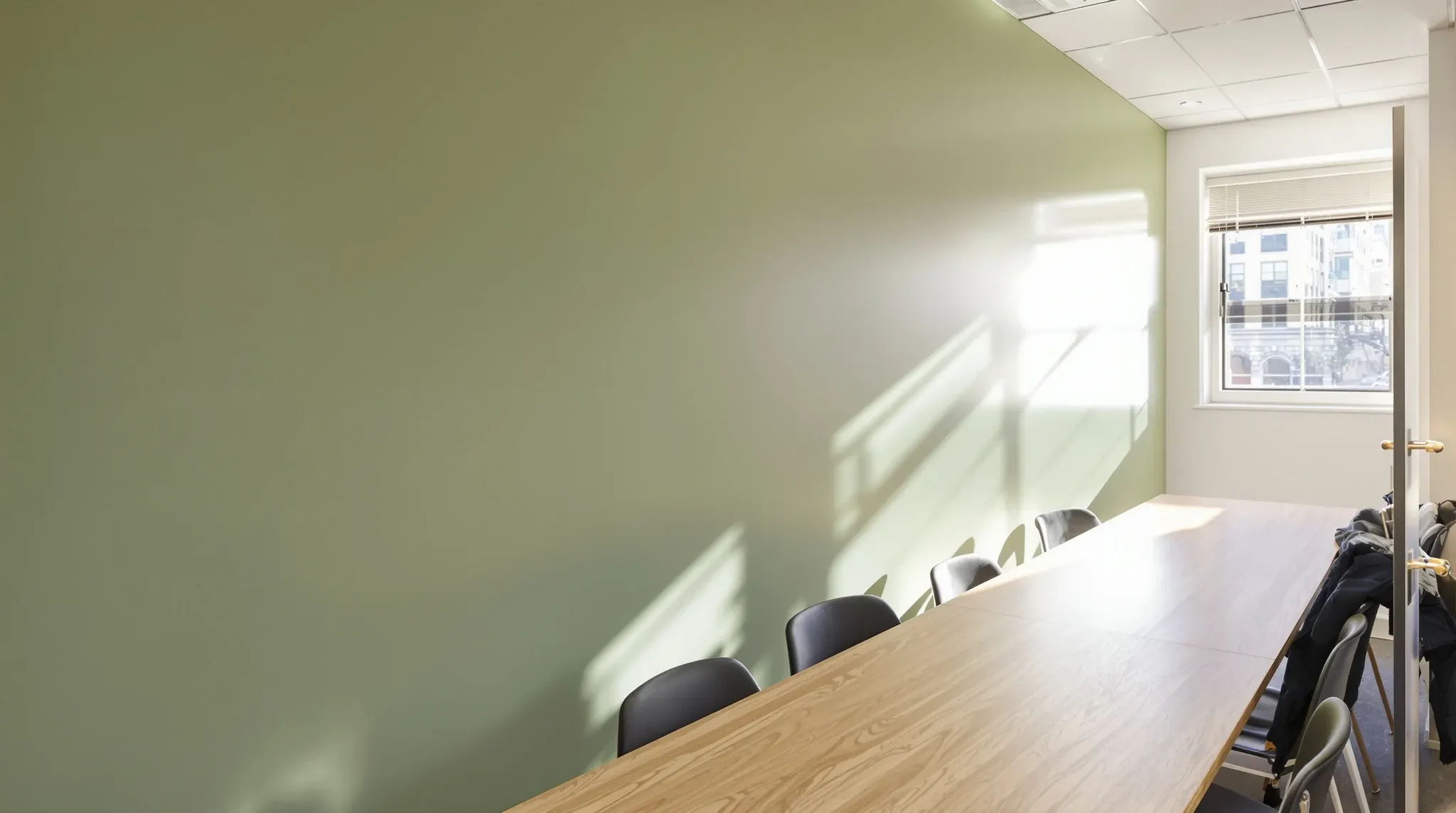 Low sun grazing along a smooth matt sage plastered wall in a small office boardroom