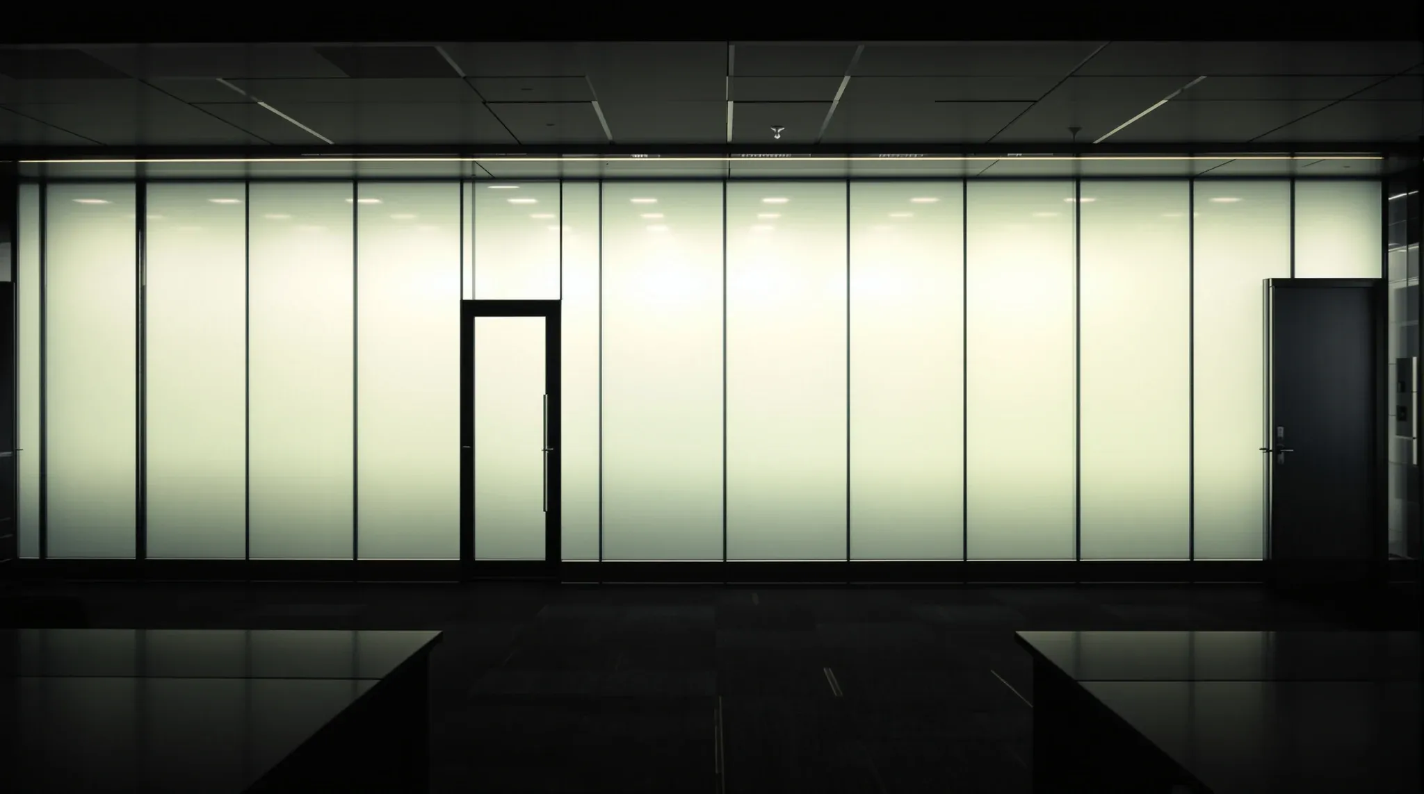 A meeting room with switchable glass turned opaque, glowing white in a dark office at night