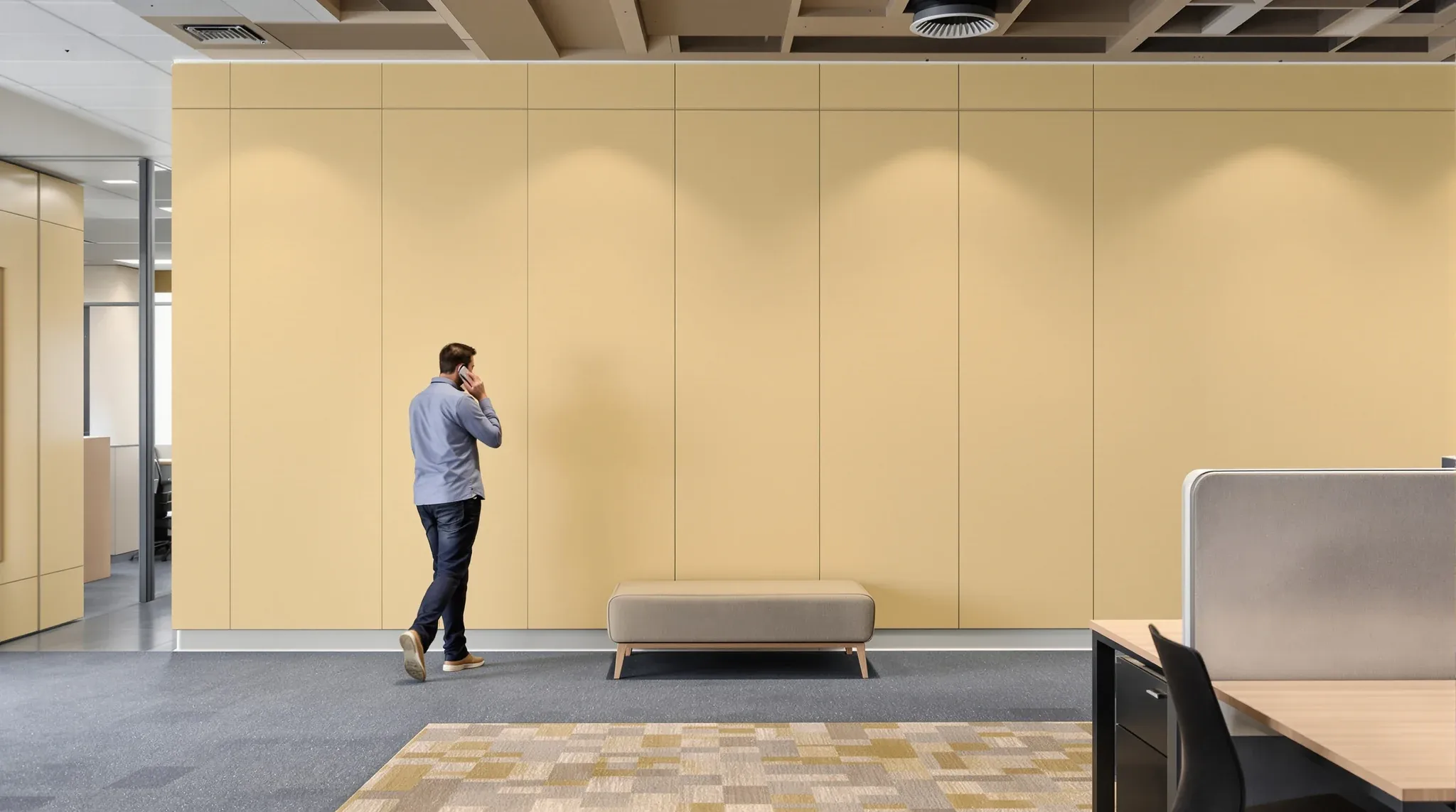 A person on a phone call leaning against a solid painted wall at the end of a desk row