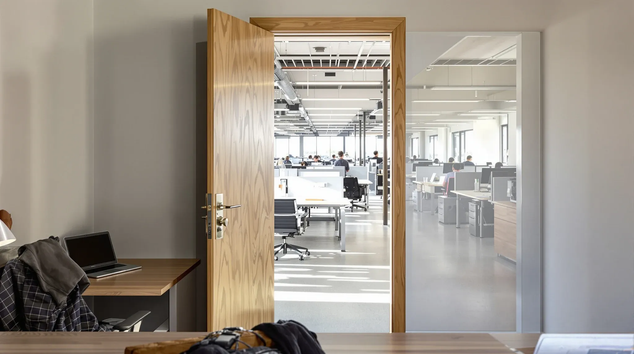 Open-plan desks seen from the doorway of a small private office