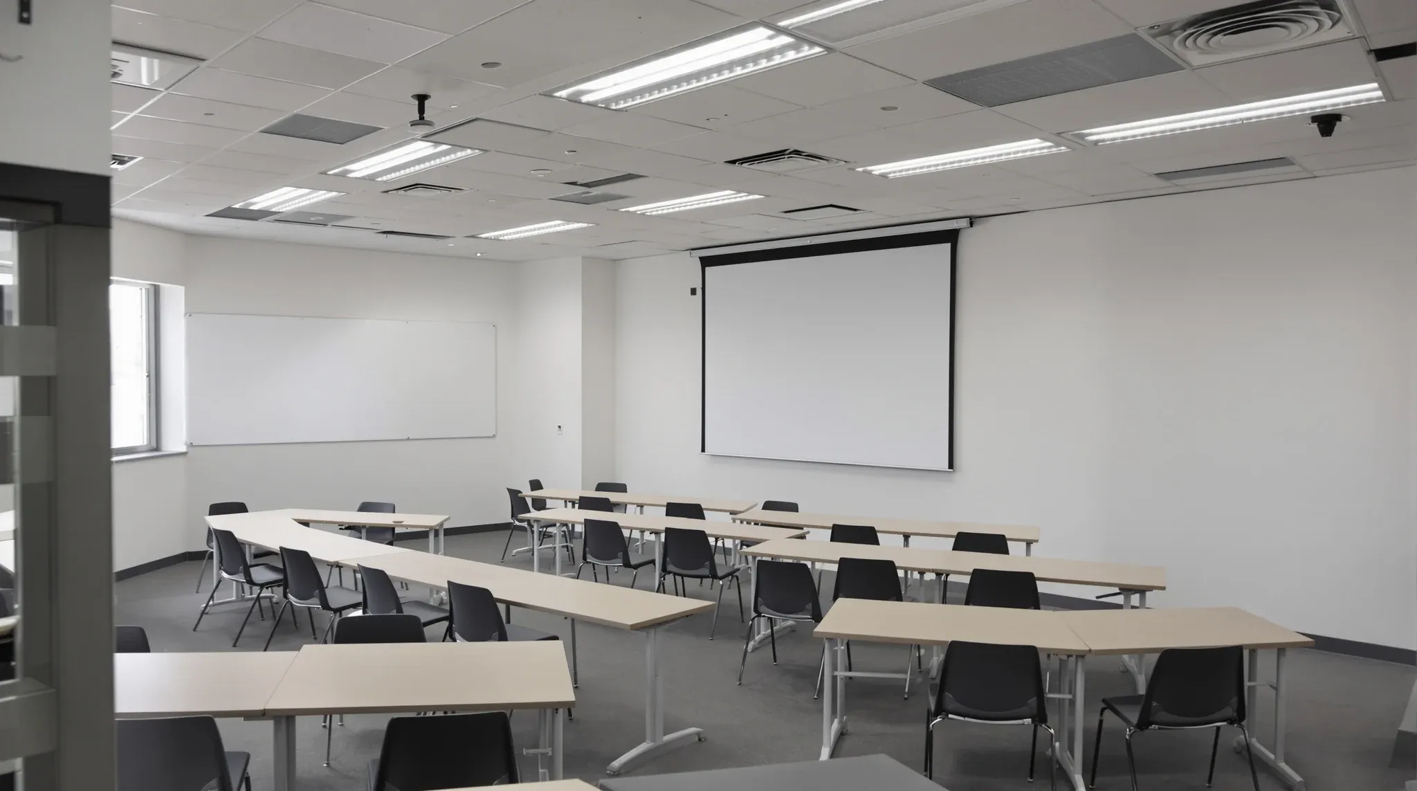 Empty finished modern classroom with tables, wall screen off, acoustic ceiling, no text on walls