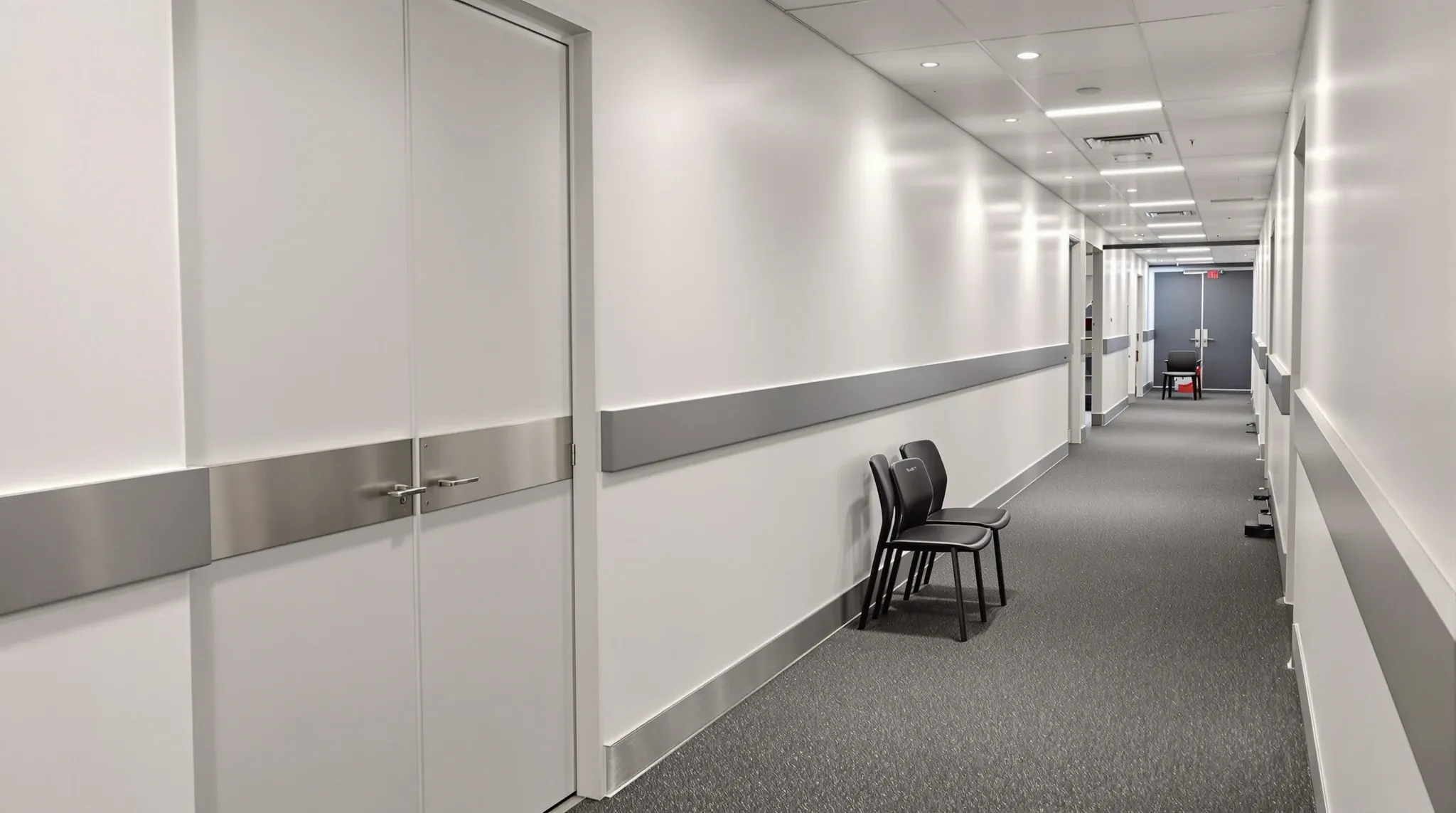 An office corridor with charcoal buffer rails on painted walls and steel kick plates on a pair of doors