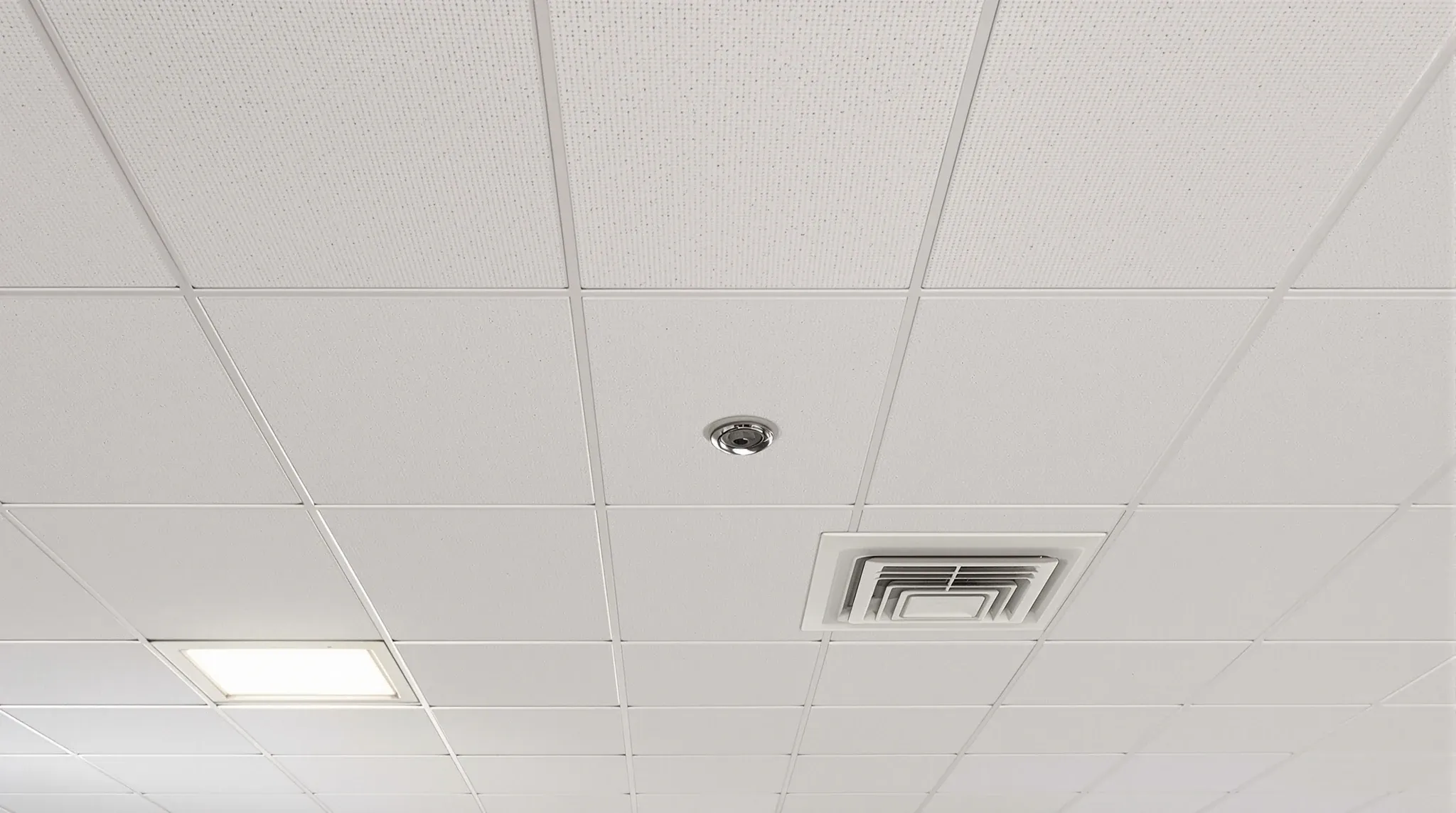 Looking straight up at a tile ceiling with lights, a sprinkler, an air diffuser and a detector neatly aligned