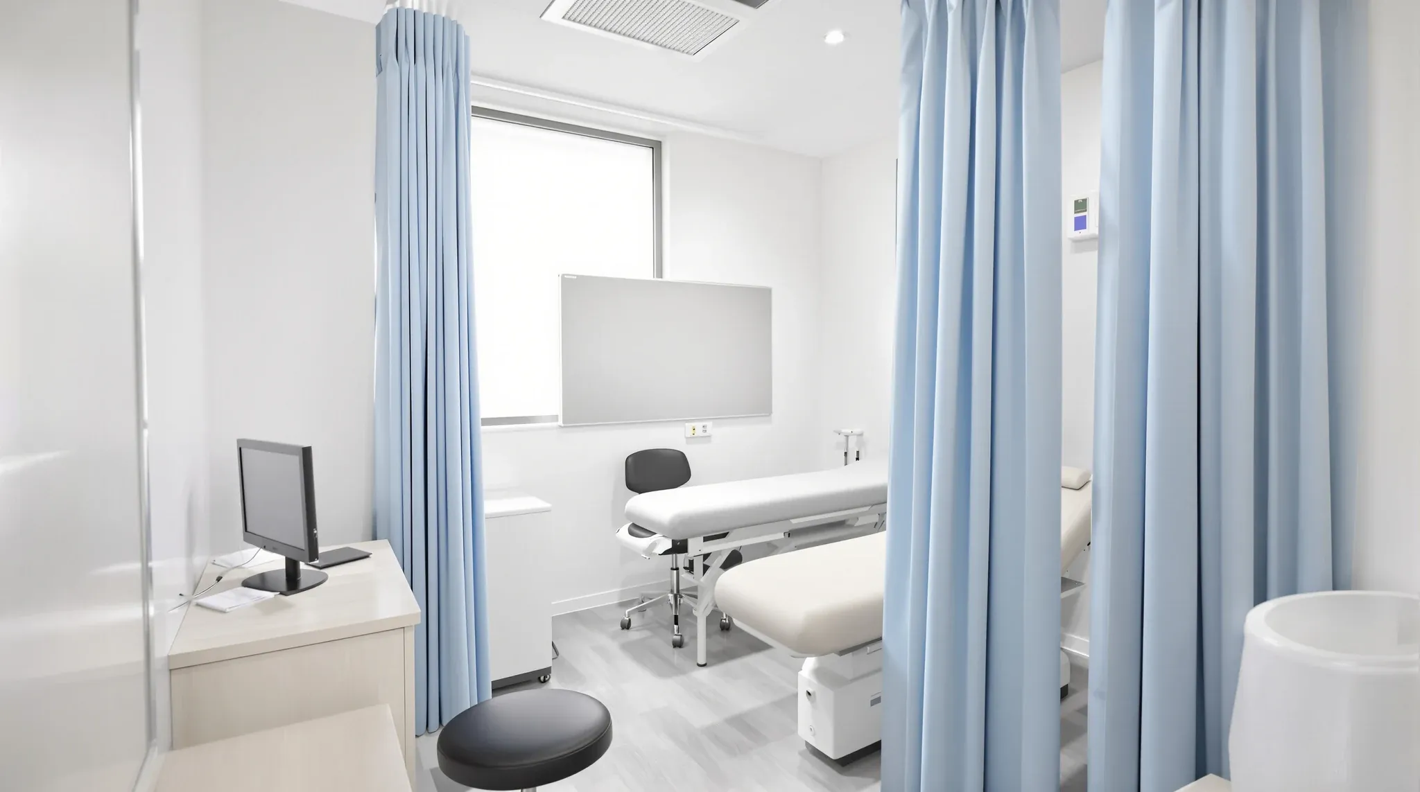 A small enclosed GP consulting room with solid walls, an examination couch and a privacy curtain