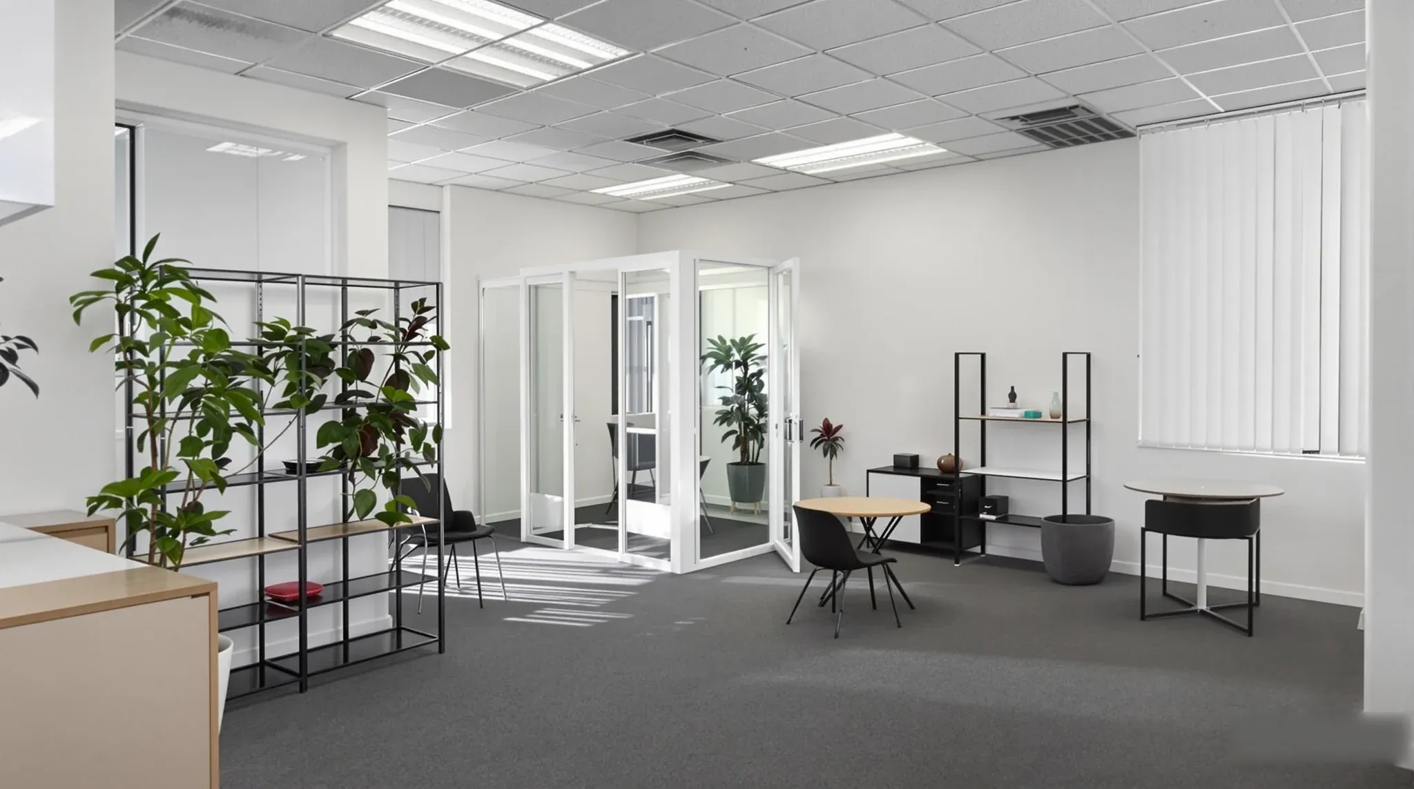 A compact office keeping its existing ceiling and carpet, organised with freestanding furniture