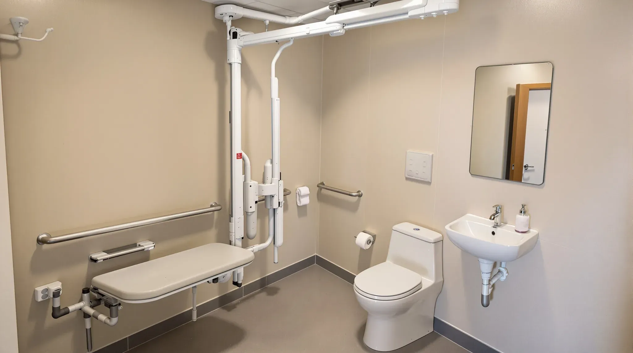 Accessible change room with a ceiling hoist, a fold-down change bench, grab rails, a toilet and a basin