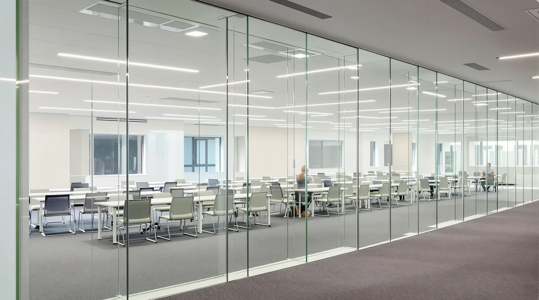 A training room behind a run of very tall frameless glass panels, seen from an office walkway