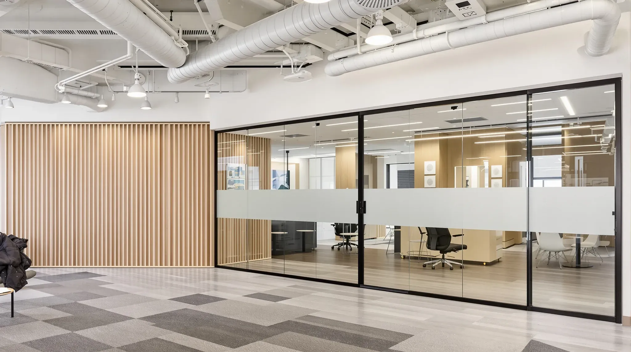 Glass meeting room with a frosted band beside a timber slat wall, under an open ceiling with exposed ducts