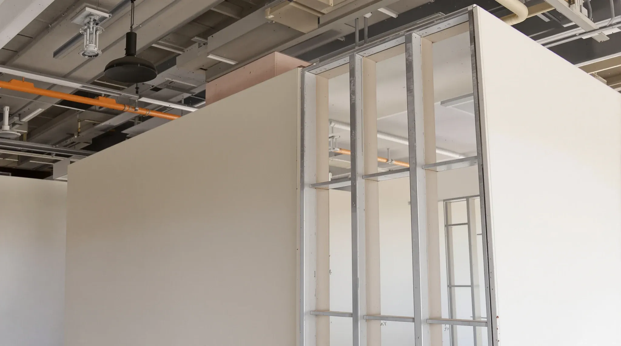 Close-up of a plasterboard partition end showing steel studs and two board layers, unfinished