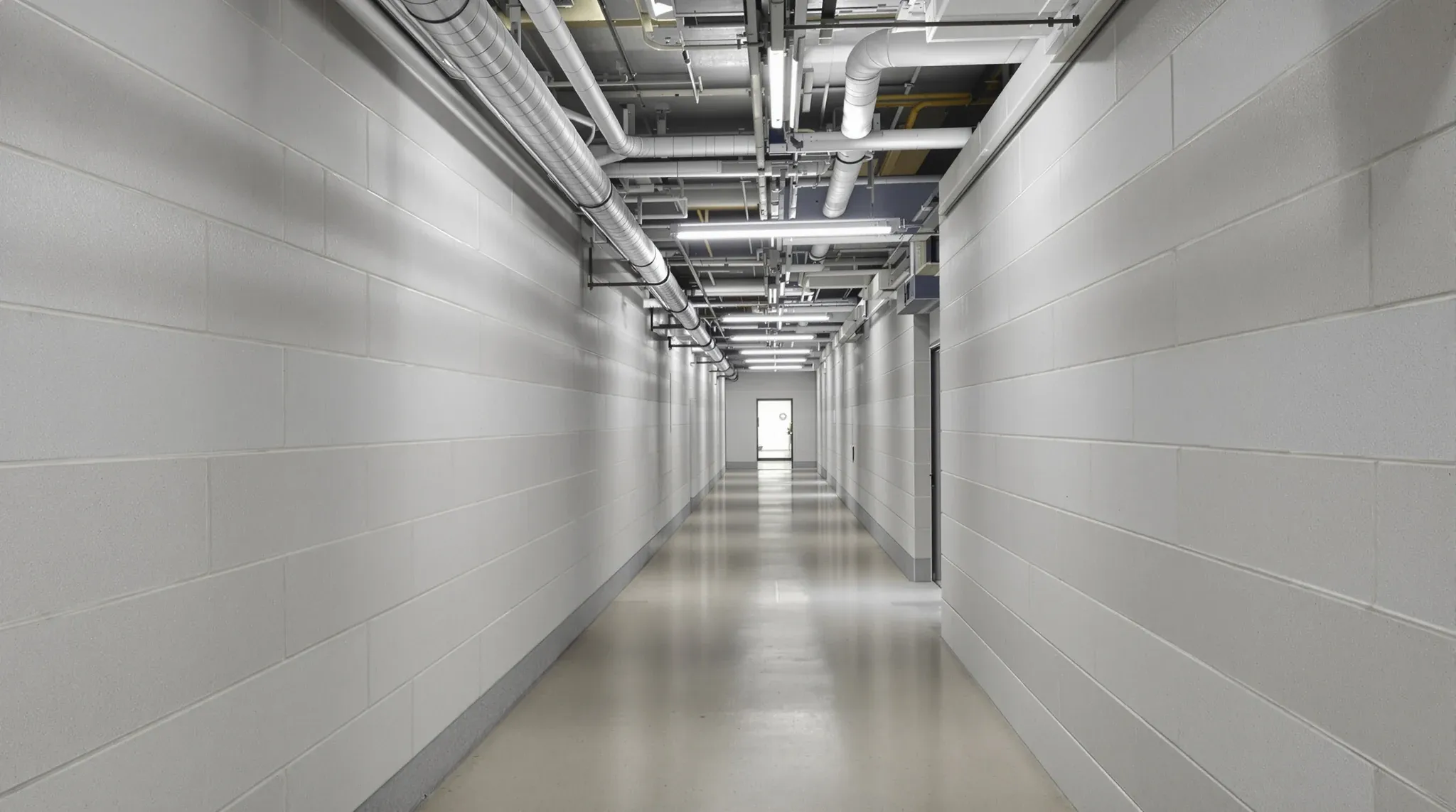 A plain basement services corridor with ceiling services visible in the distance