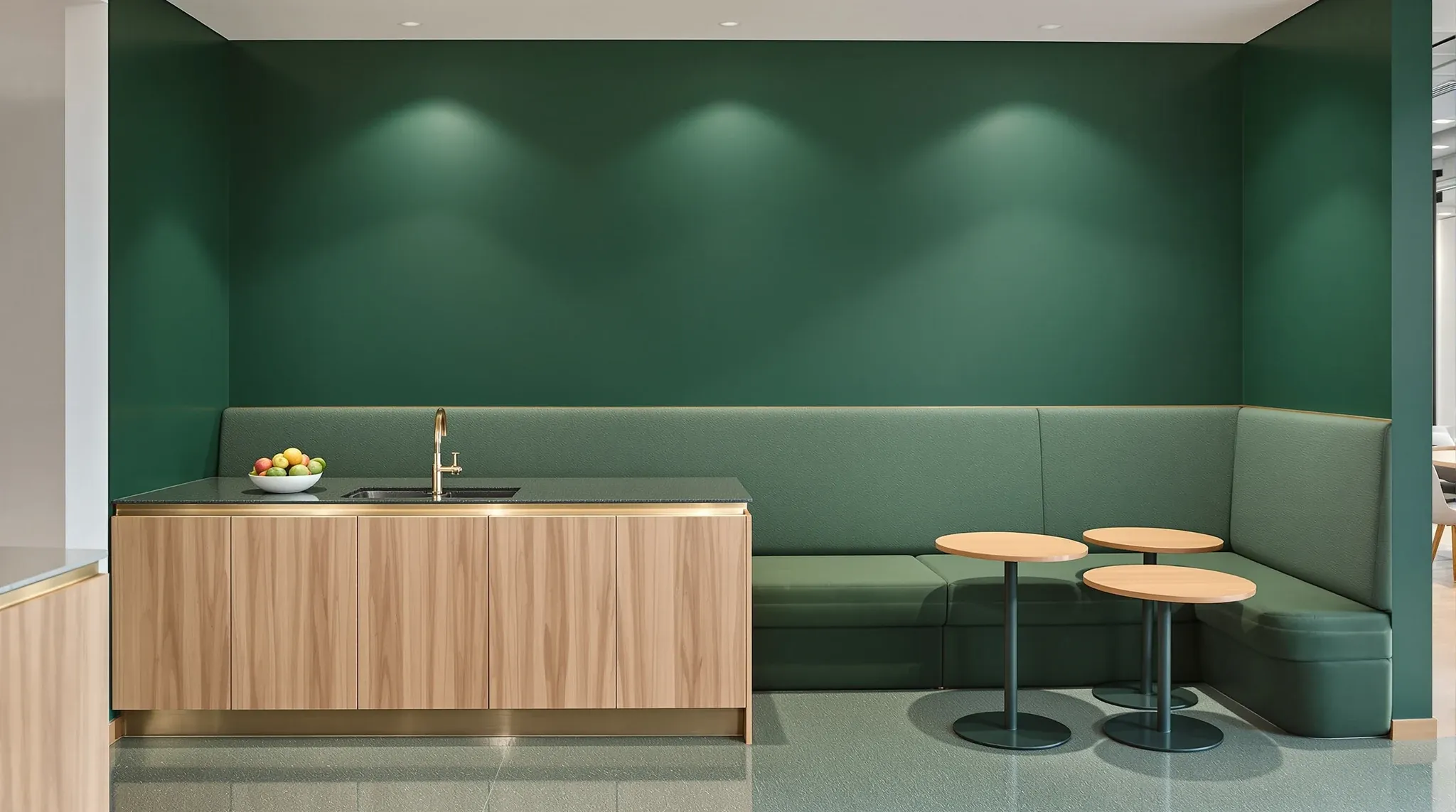 An office tea point in bottle green with a terrazzo bench, brass trim and a green banquette beside it