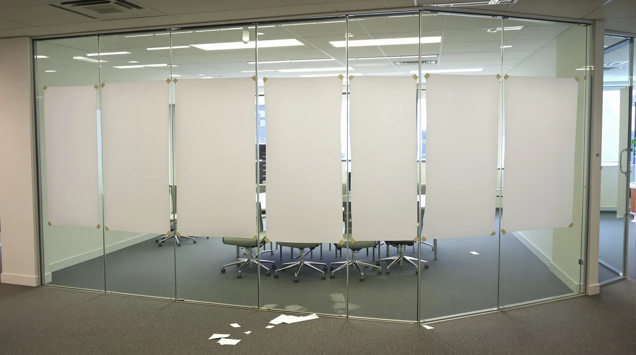 Sheets of blank paper taped inside a glass meeting room wall for privacy