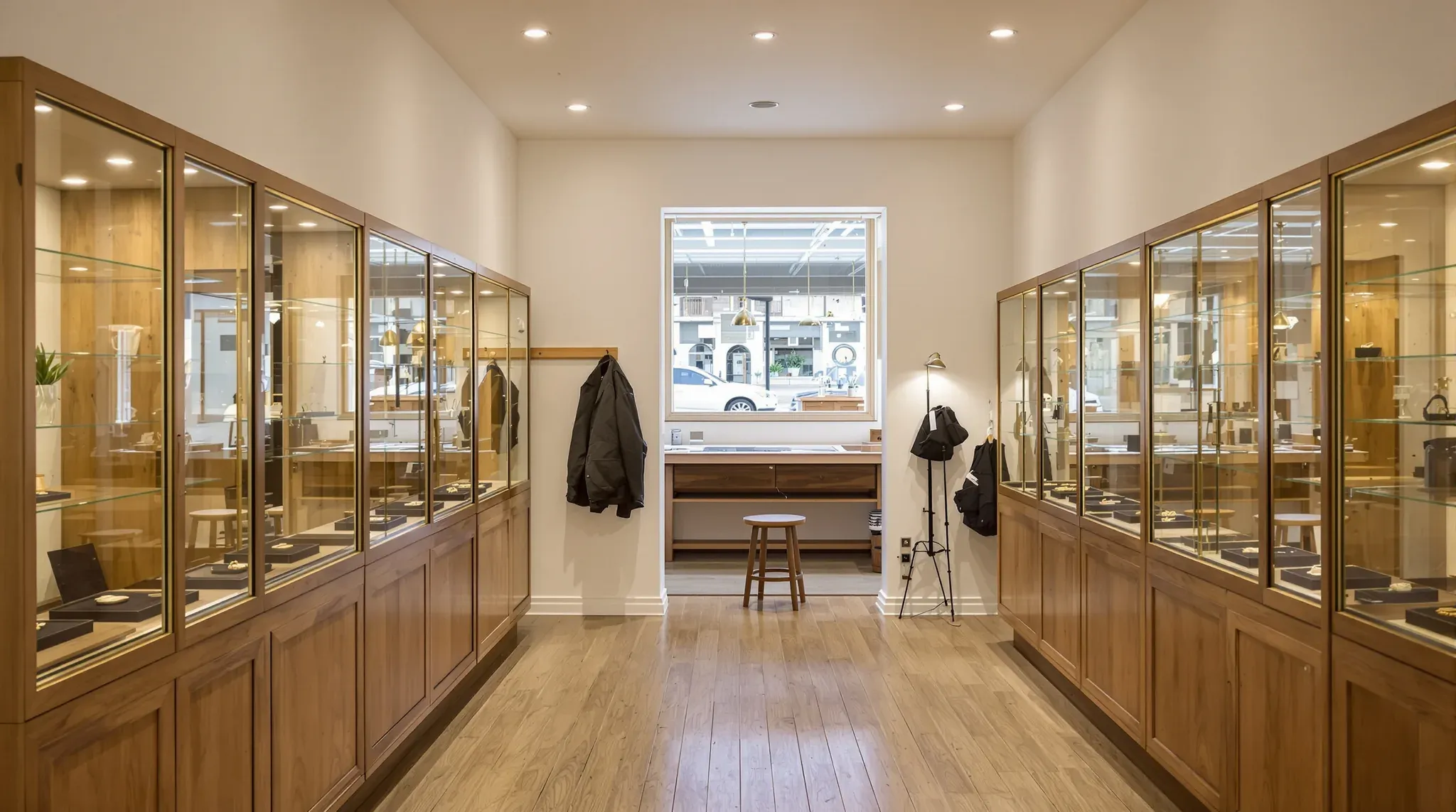 Jewellery store with lit timber and glass display cases on both sides and a workbench under a back window