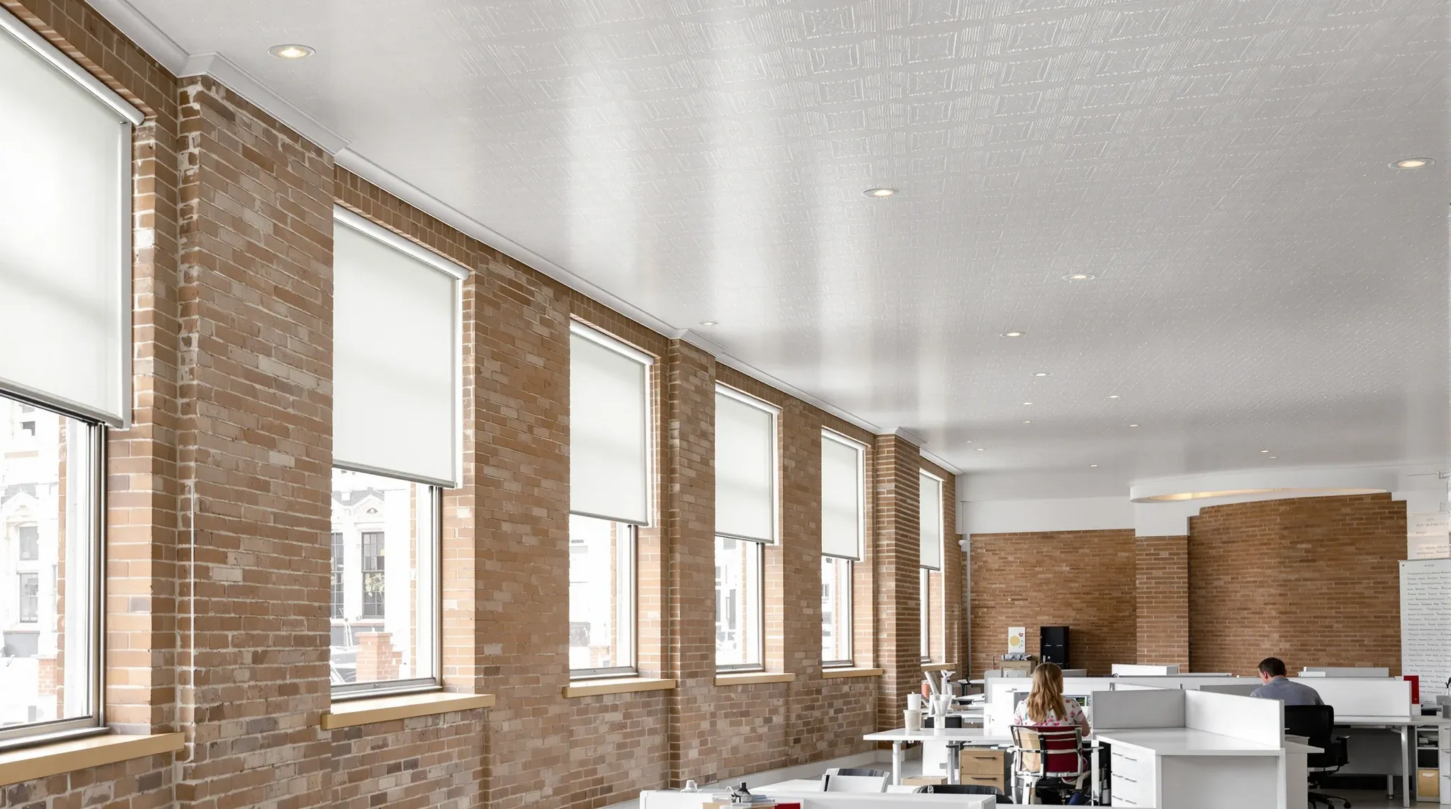 An office in an 1890s building with a white pressed metal ceiling, tall blind-covered windows and modern desks