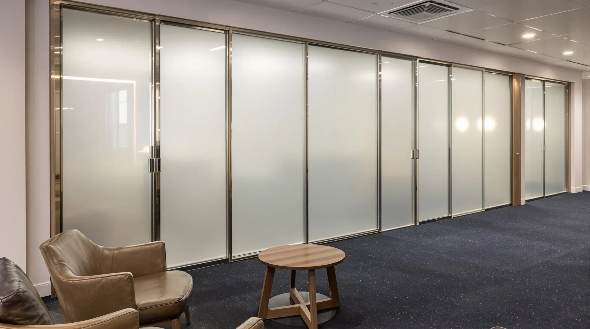 A row of meeting rooms with frosted glass fronts seen from a small client lounge