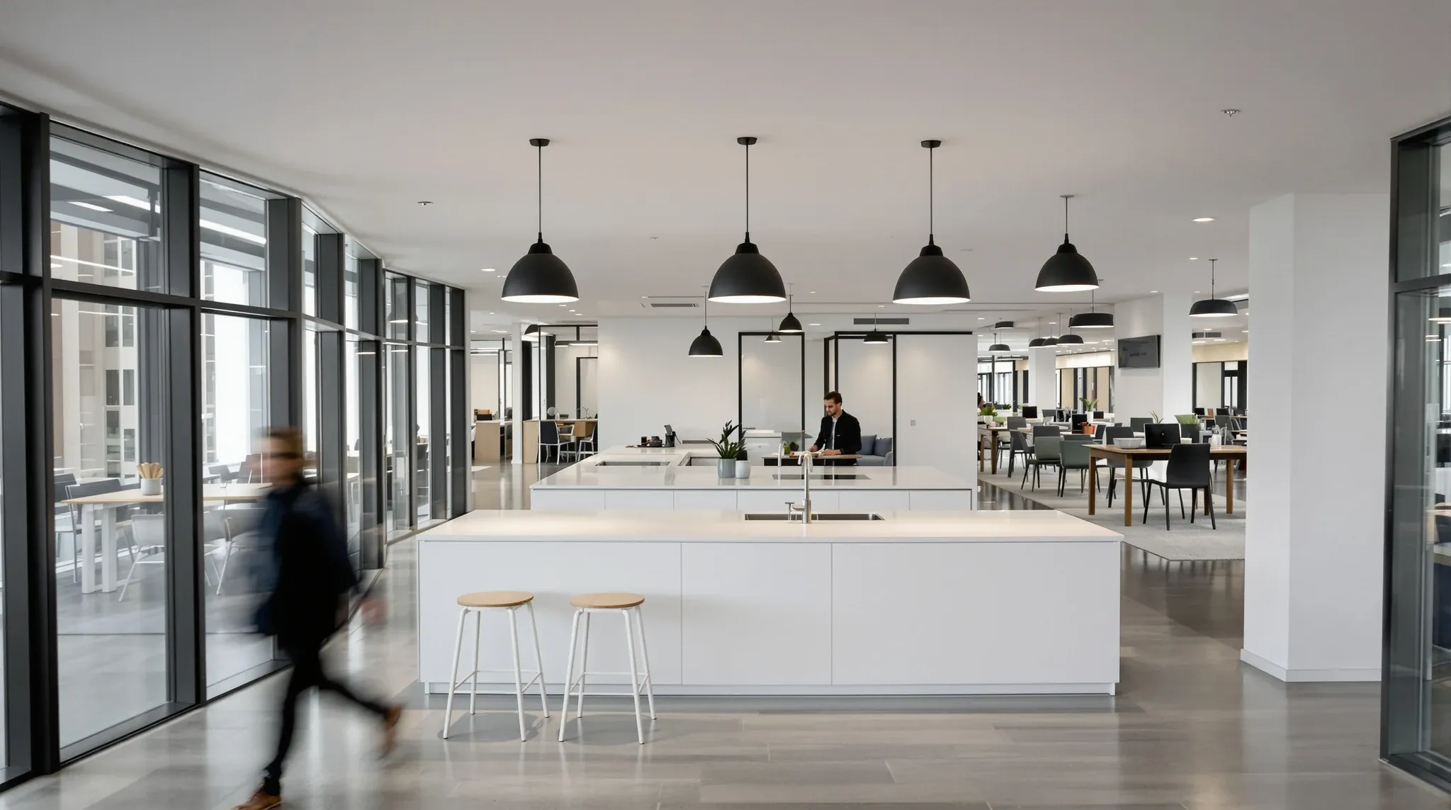 An office kitchen island where two walkways cross, with team tables and rows of desks around it