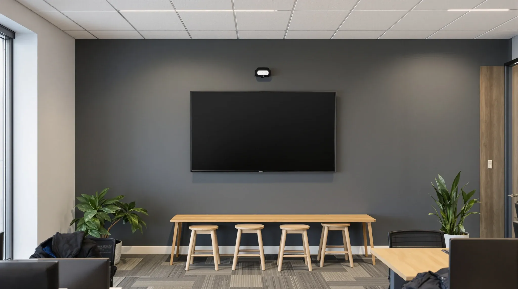 A large wall screen with a small camera above it at the end of a team area in an established office