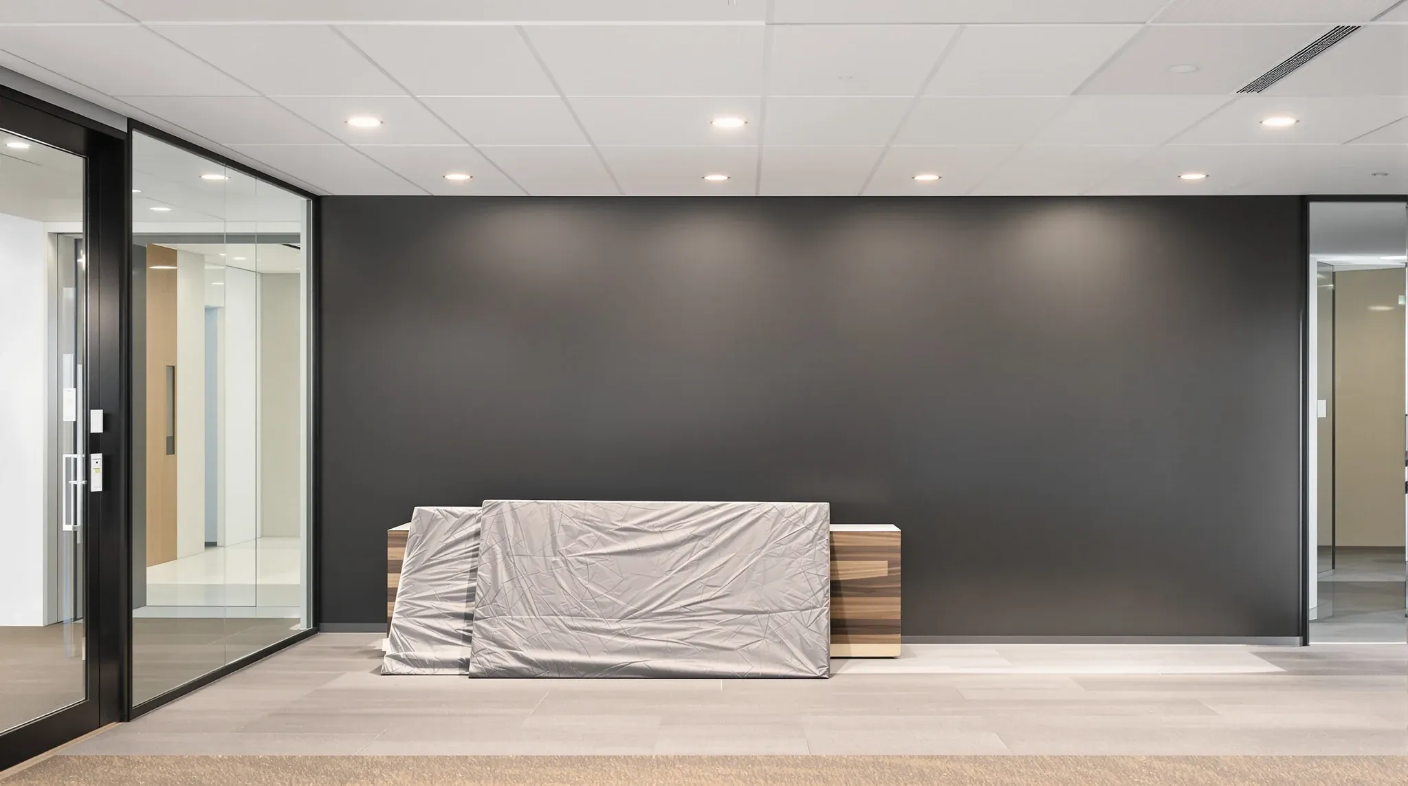 A removed reception sign panel wrapped in a blanket, leaning below a freshly painted blank wall in an empty office
