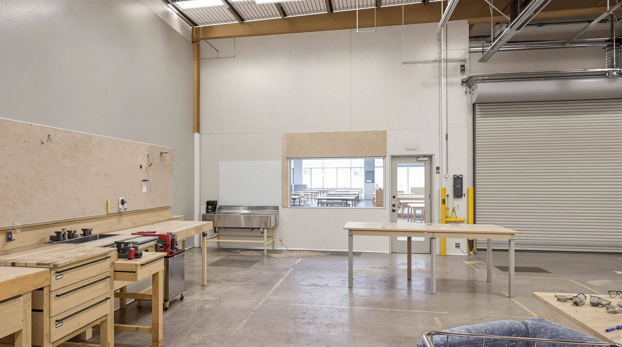 Trade training workshop with timber benches and vices, a sink, a viewing window and a roller door