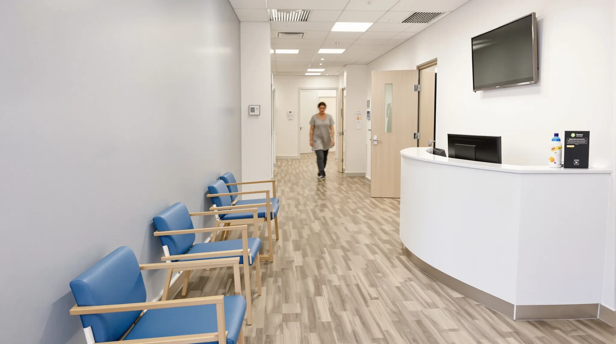 A health practice waiting area with a clean row of wipeable chairs, a vinyl floor and an unattended counter