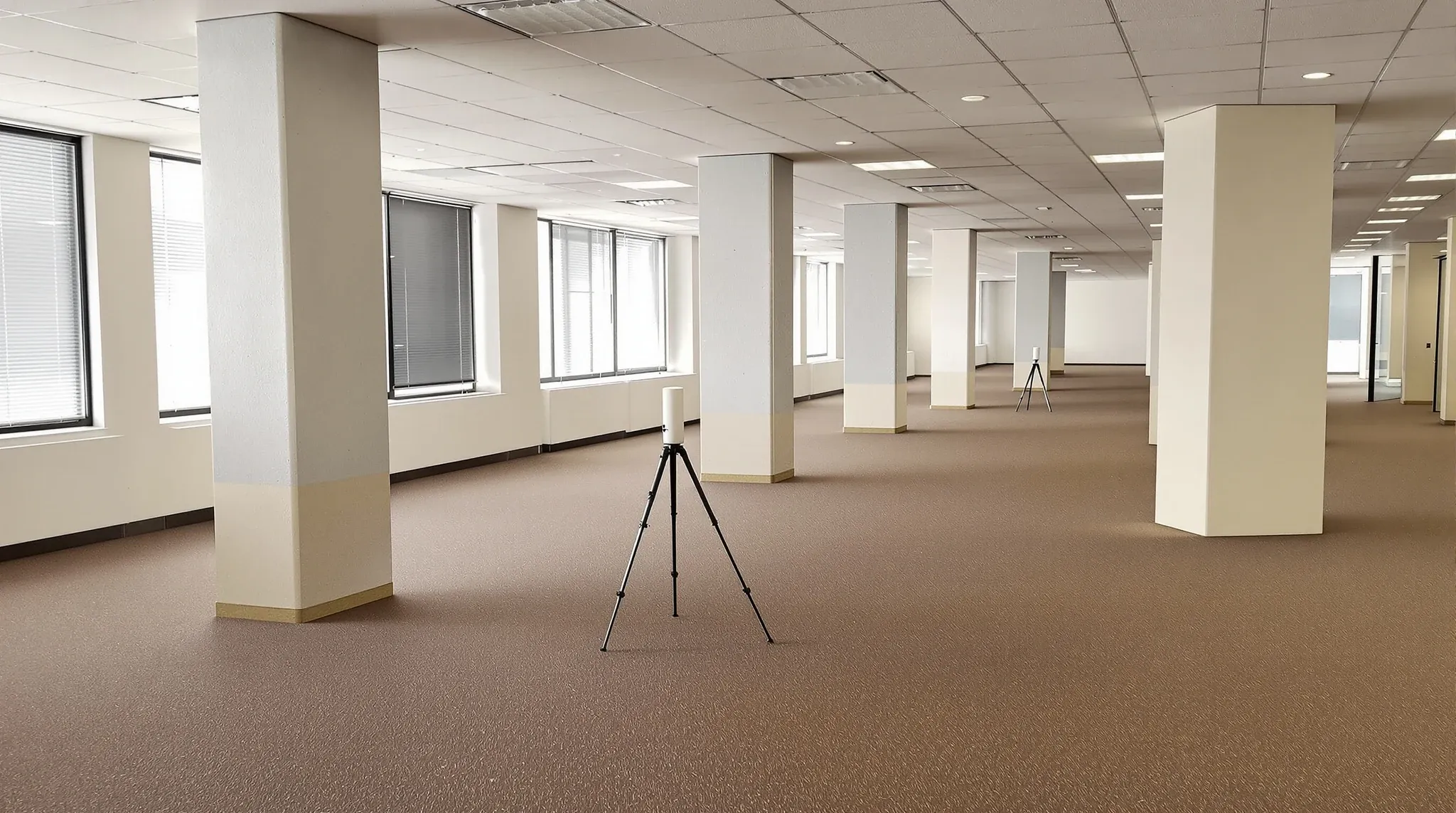 A 3D laser scanner on a tripod in the middle of an empty older office floor