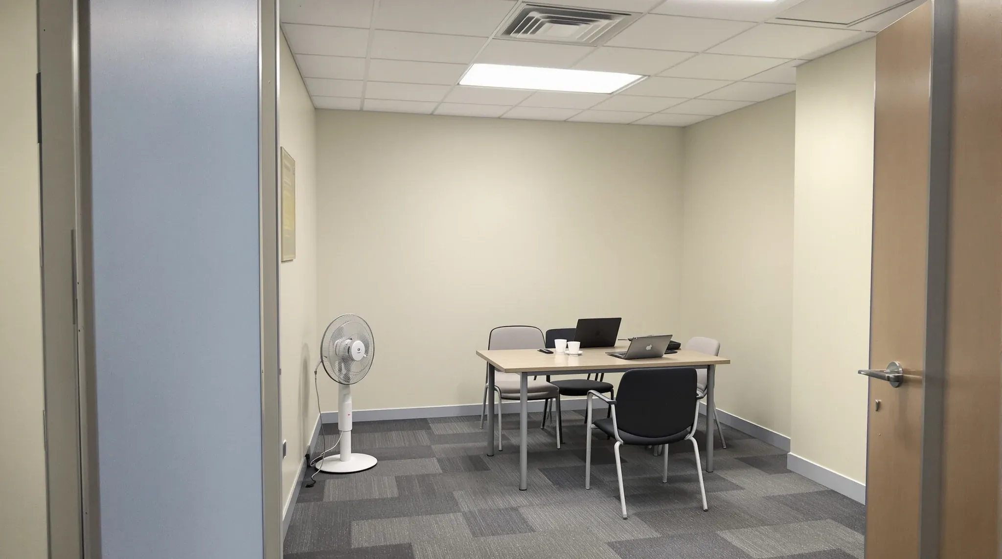 A stuffy small internal meeting room with a pedestal fan on the floor and scuffed walls