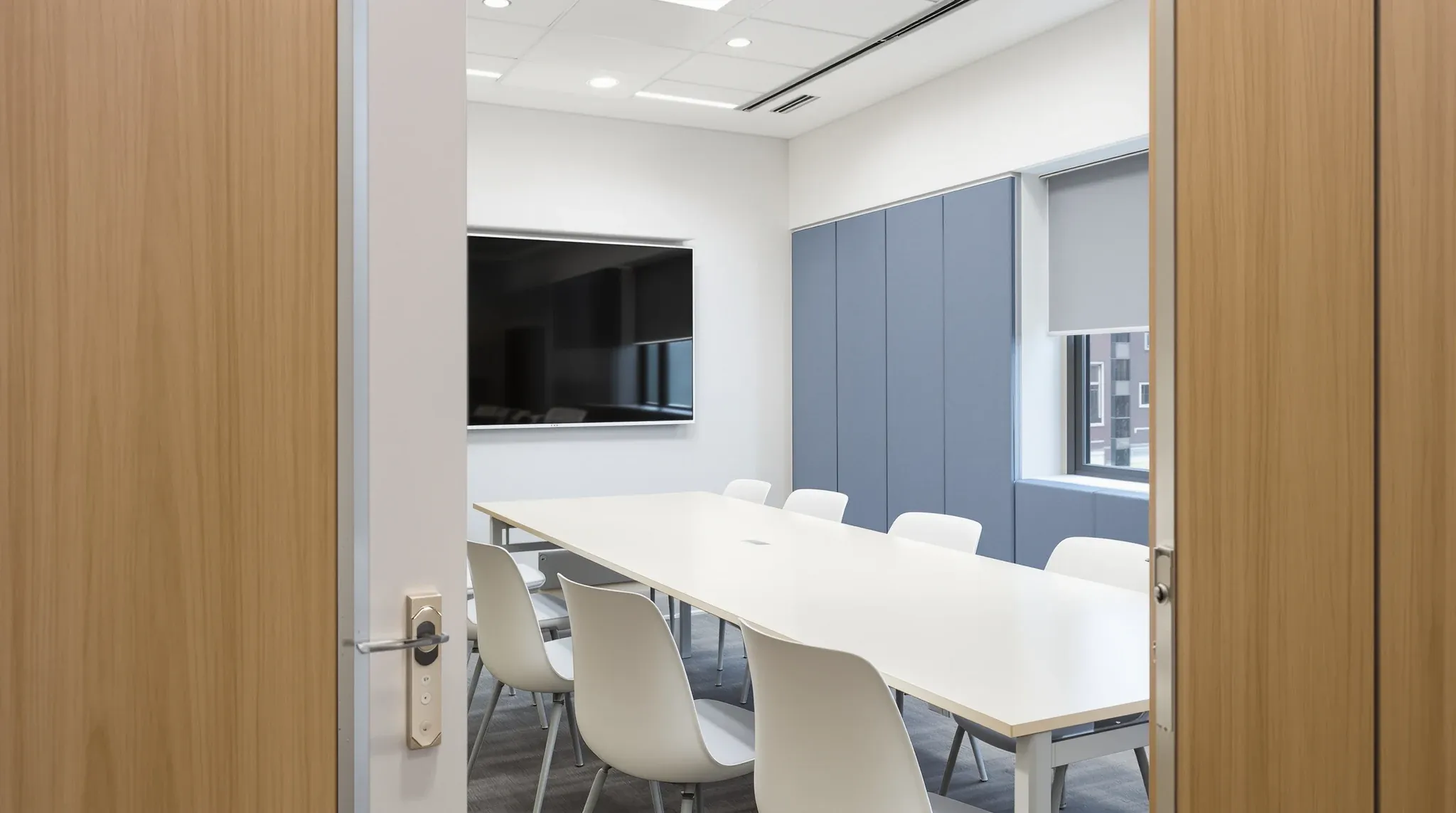 An enclosed plasterboard meeting room with fabric wall panels, a dark screen and evenly spaced chairs