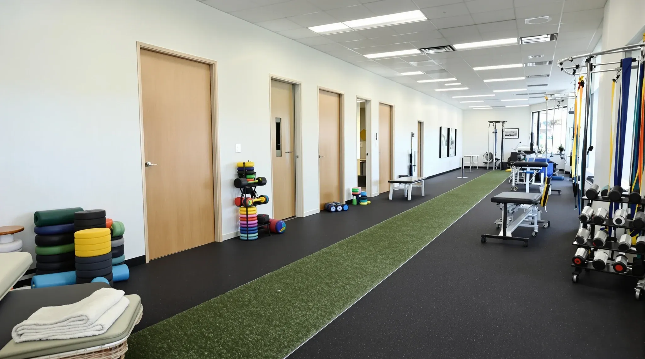Empty physiotherapy rehab area with rubber floor, treatment plinth and closed treatment room doors