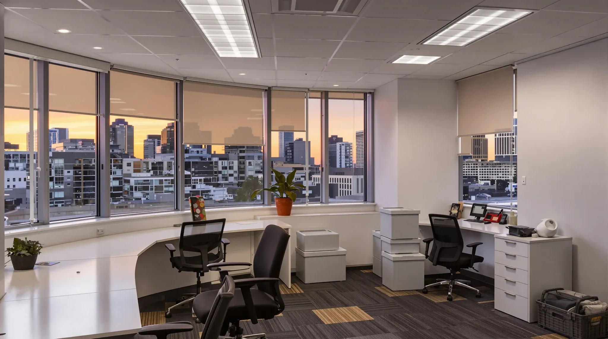 A cleared office at dusk with chairs upturned on desks and crates stacked by the door